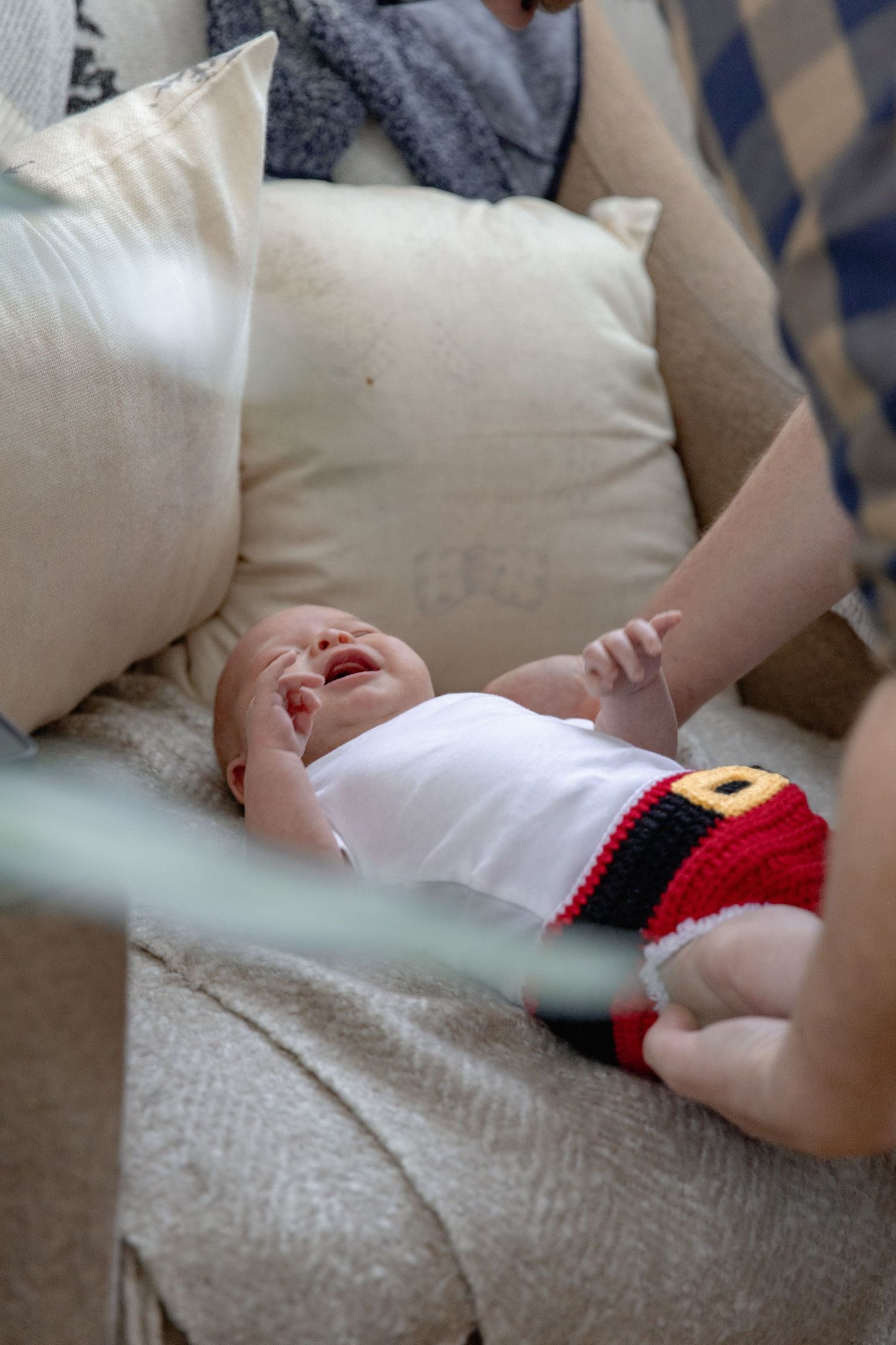 A series of photos showing a baby wearing a festive red and black Santa outfit while lying on a beige couch.