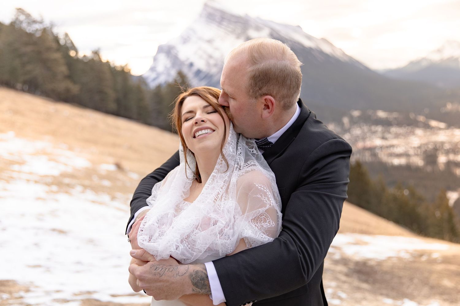 A couple embraces lovingly in front of a snowy mountain landscape during a winter wedding photo session.