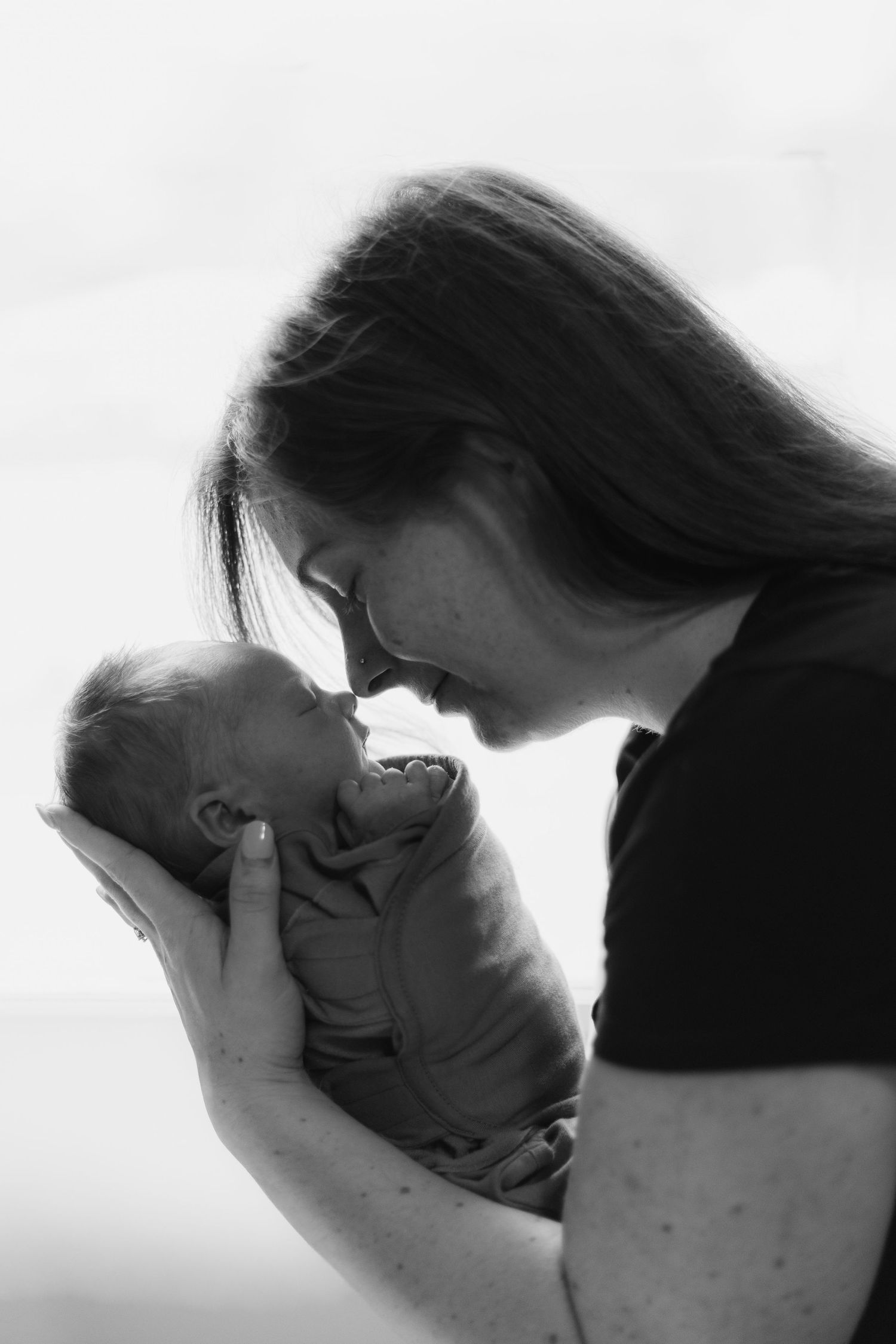Black and white portrait of a tender moment between parent and child in intimate lighting.