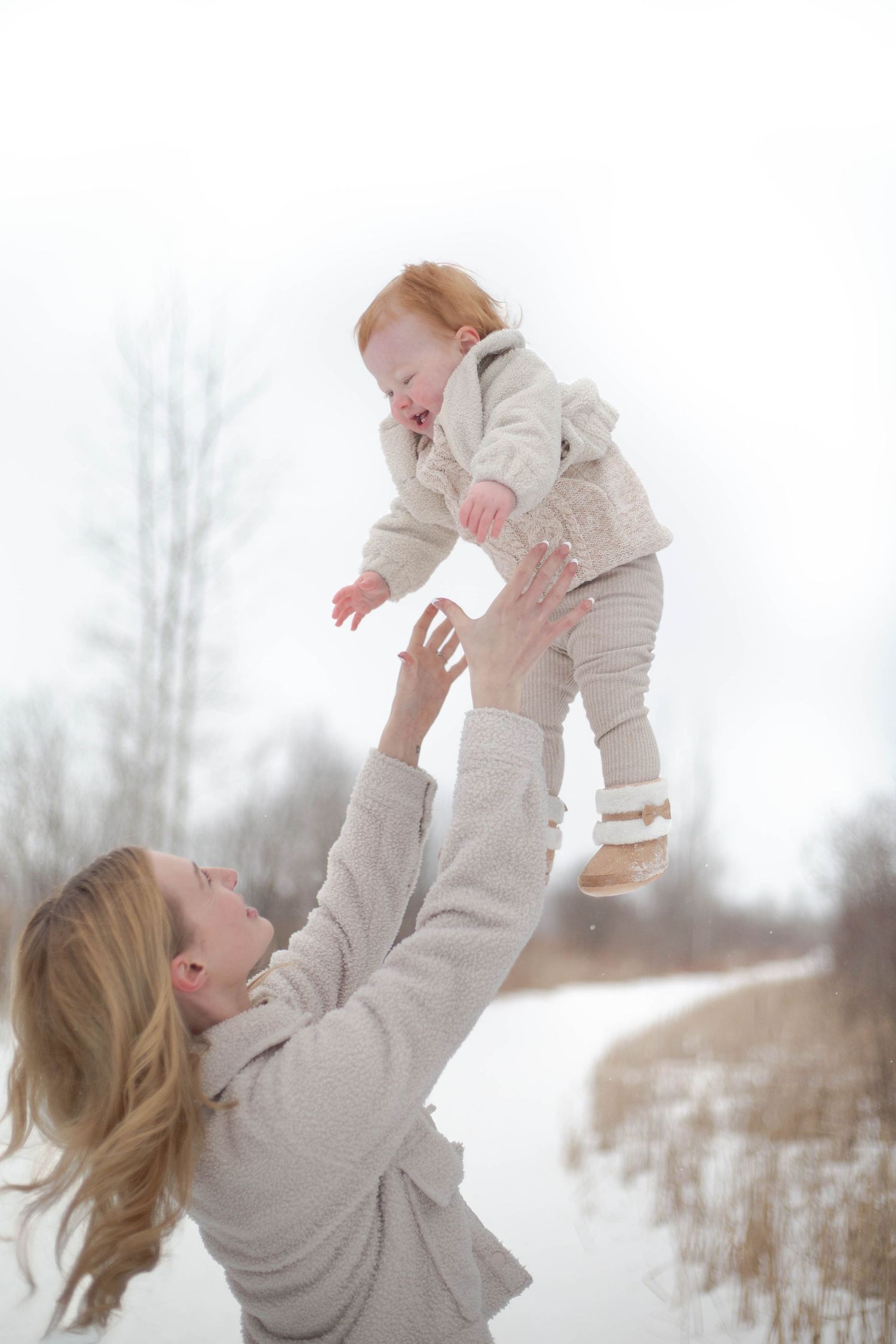 Parent tosses joyful baby high in the air against a snowy winter landscape.