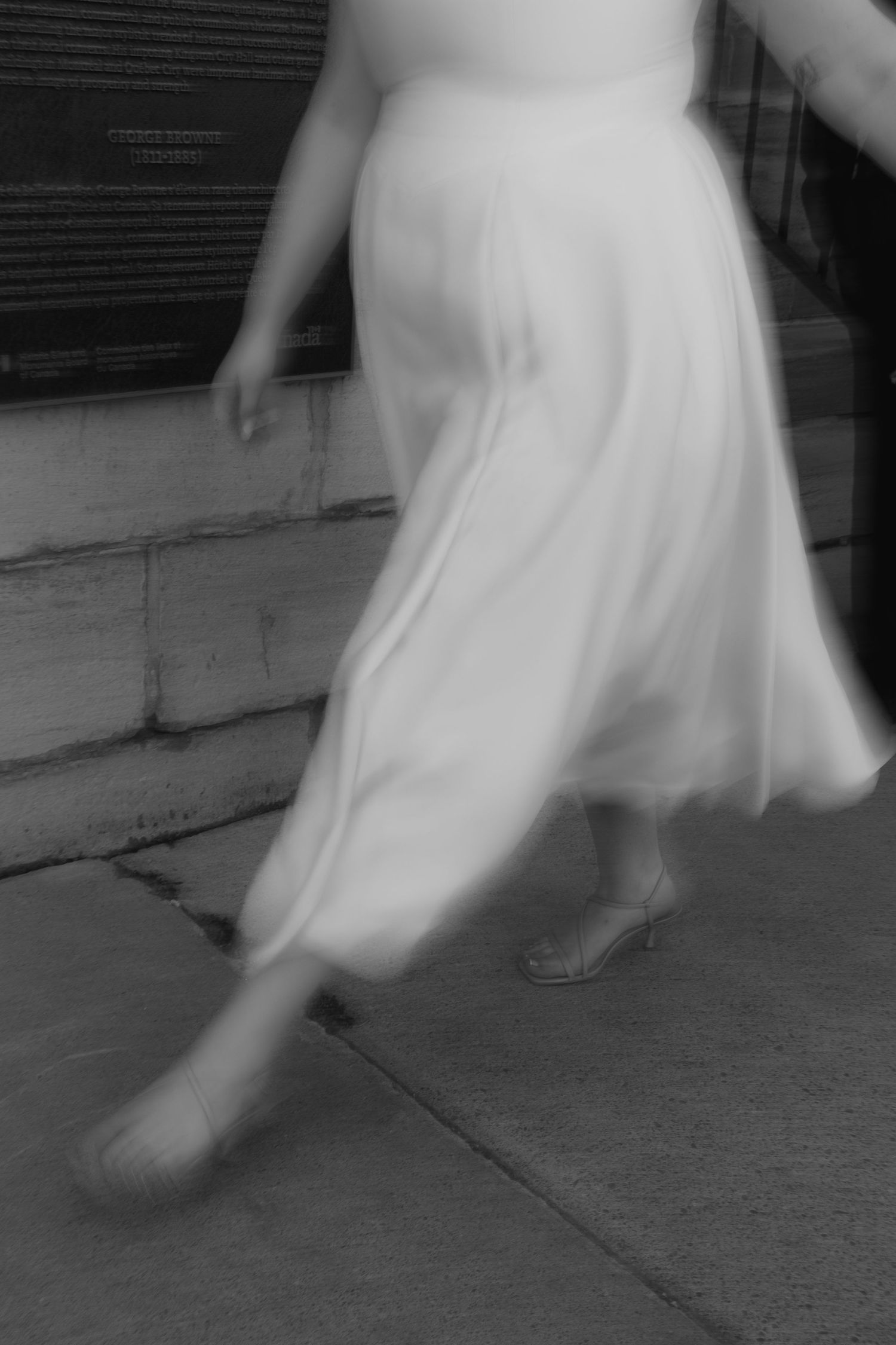 A sequence of blurred black and white photos showing the motion of a flowing white dress against a concrete background.