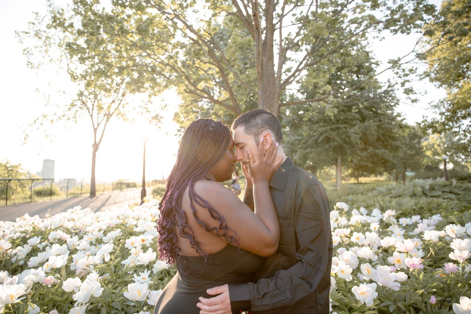 Romantic couple embraces in a sunlit garden setting with white flowering trees during a springtime photo session.