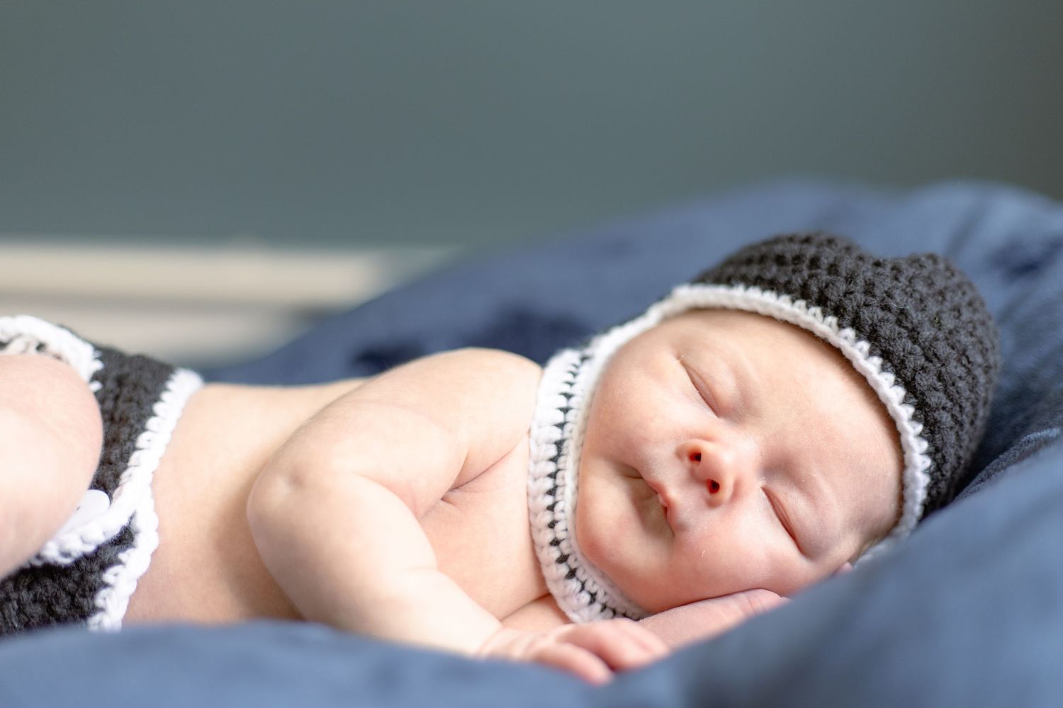 Sleeping newborn wearing a knitted black and white striped beanie hat rests on blue blanket.