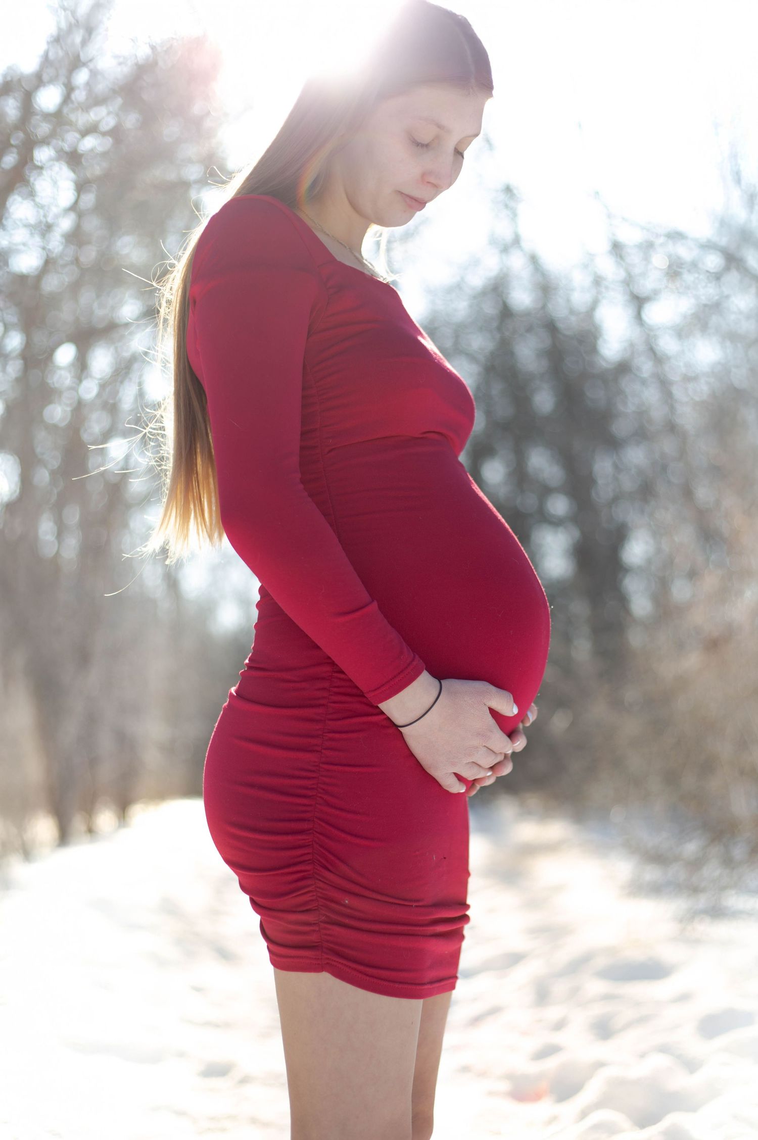 Gentle winter maternity moment captured in a crimson dress with natural lighting.