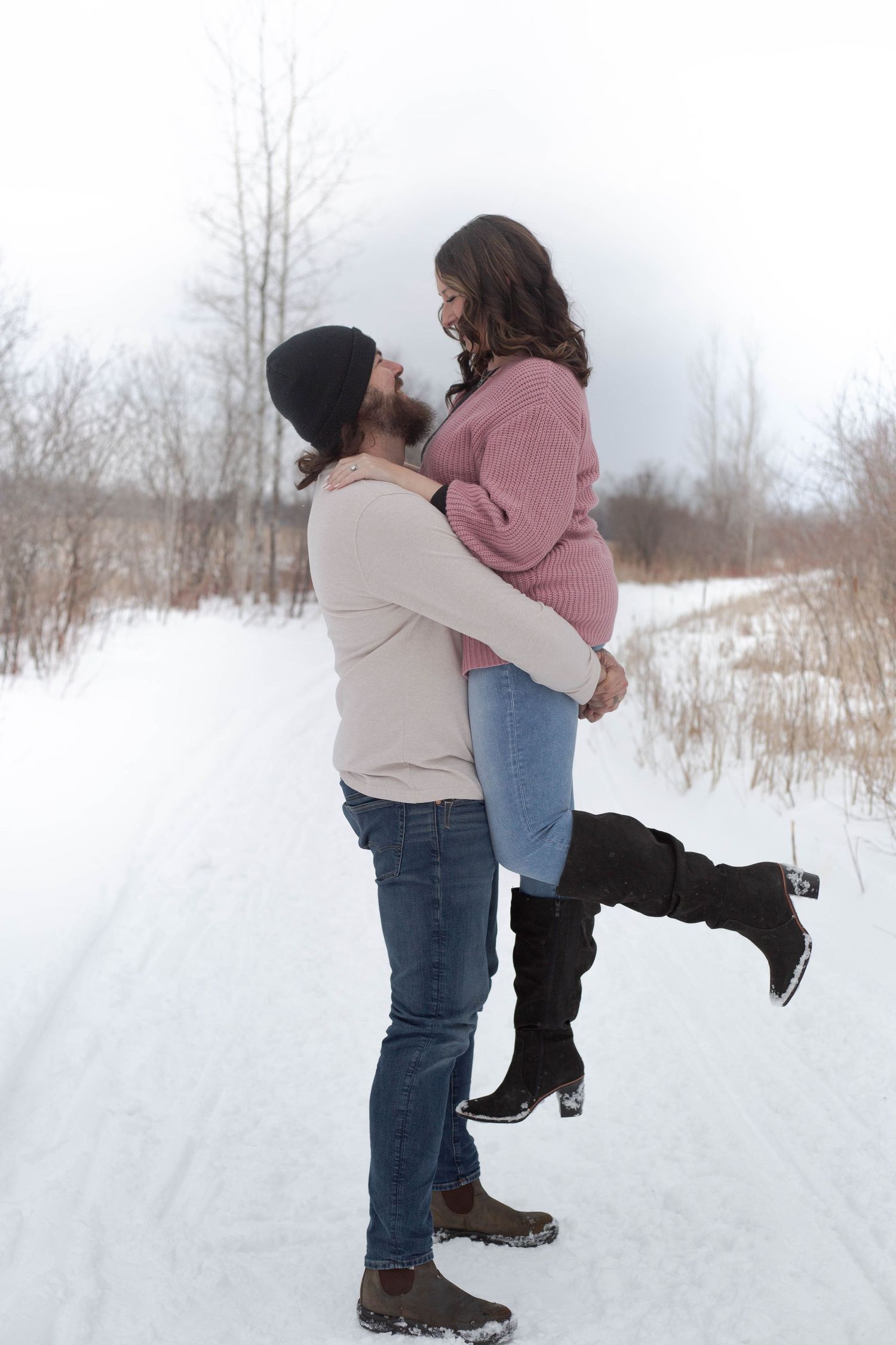 Romantic moment captured as couple embraces on snowy path with natural winter scenery.