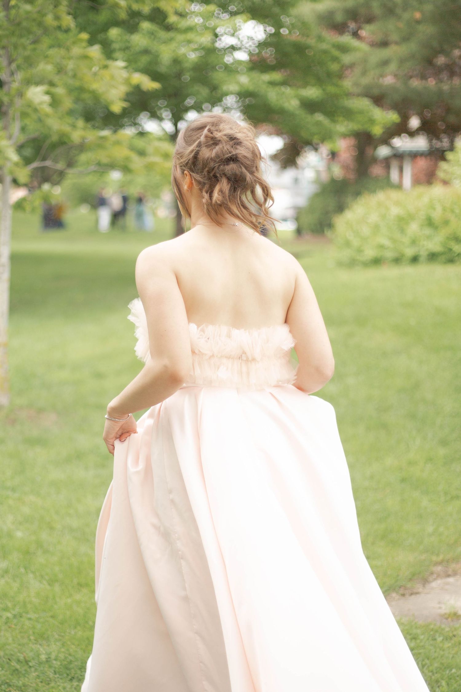 Back view of a strapless blush wedding dress against a green garden background.