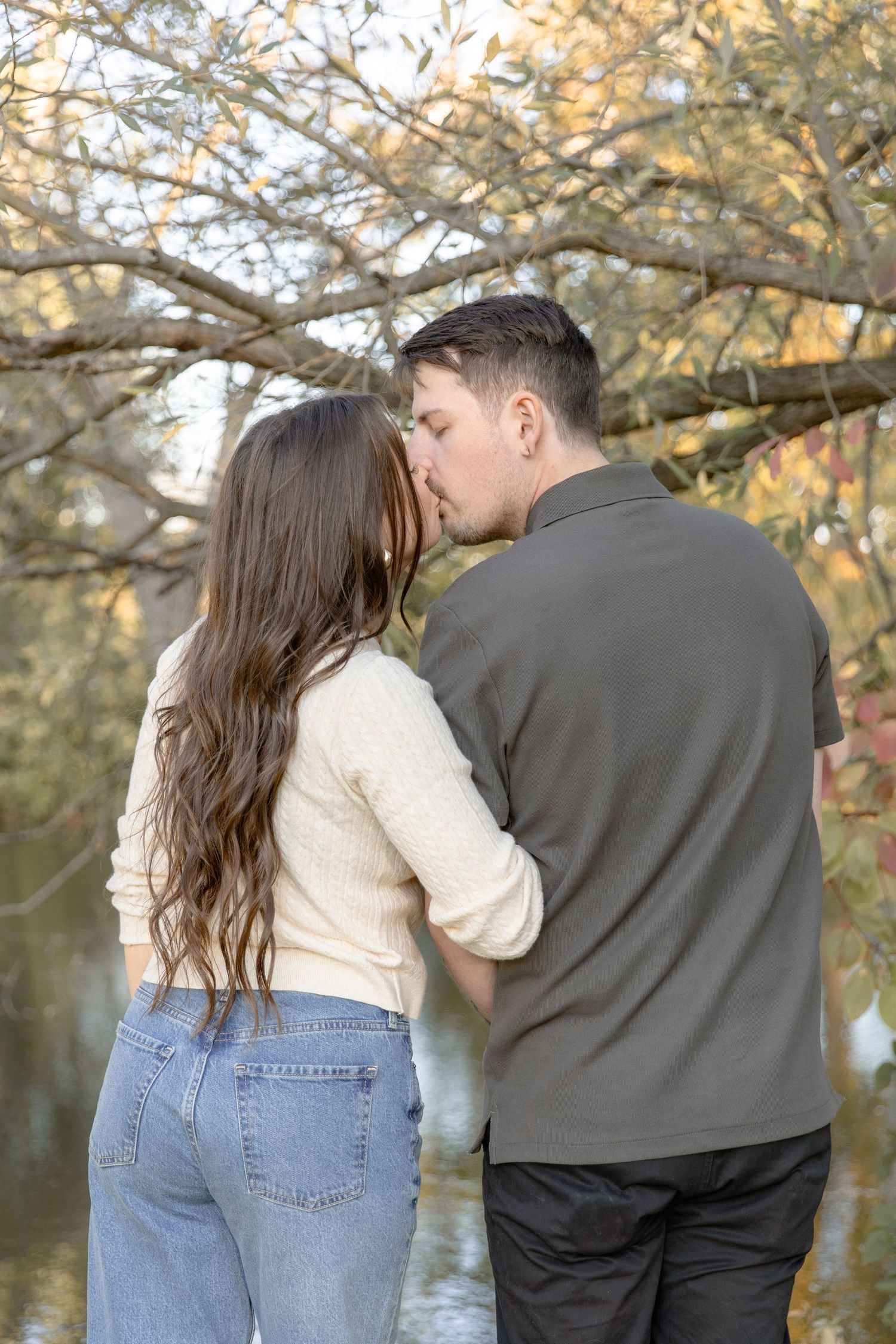 A couple sharing a romantic moment together outdoors with autumn trees in the background.