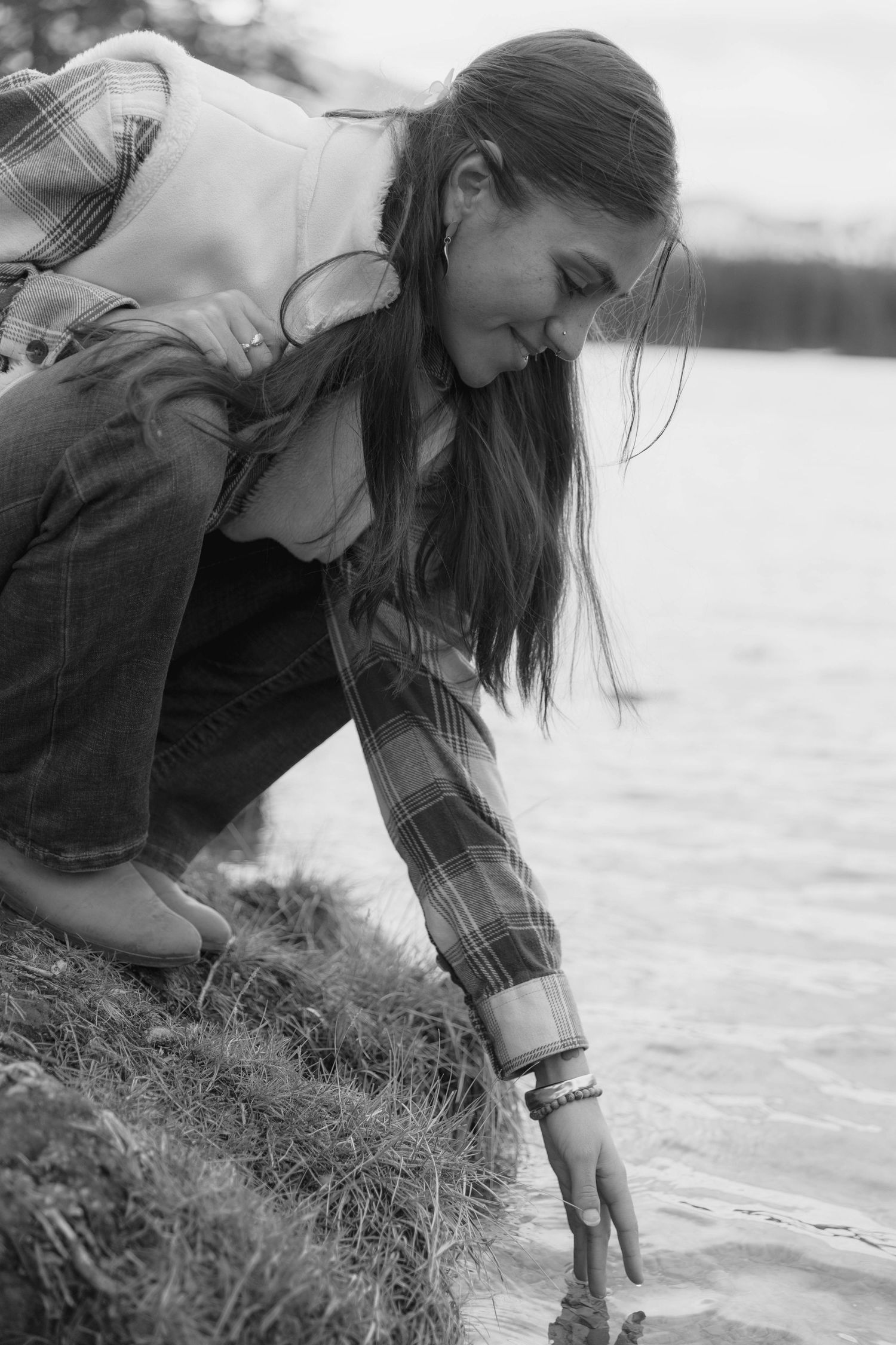 Black and white series of a woman in denim jacket exploring the shoreline and reaching toward the water's edge.