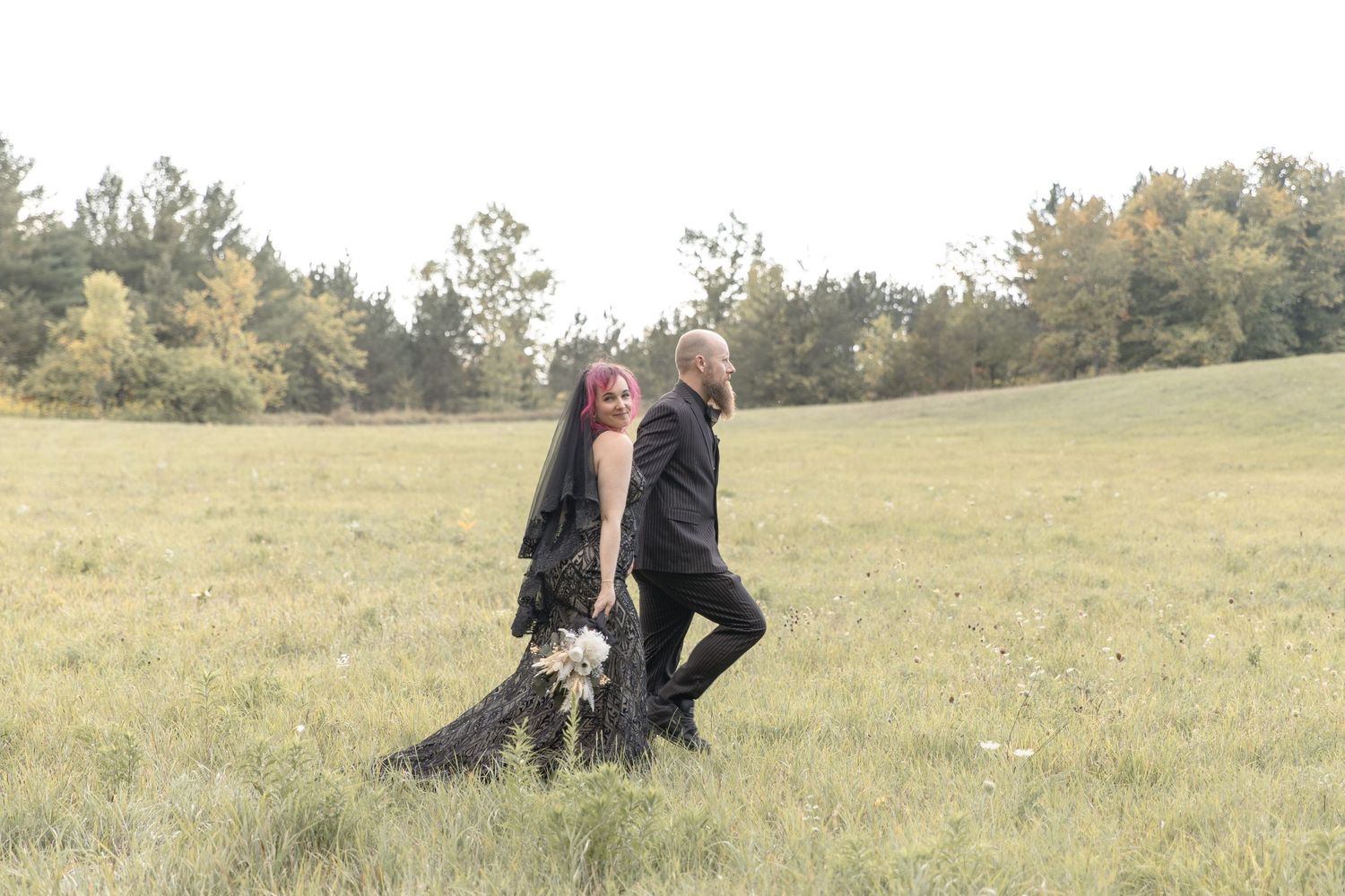 Two people and a dog playing together in a grassy meadow on an autumn afternoon.