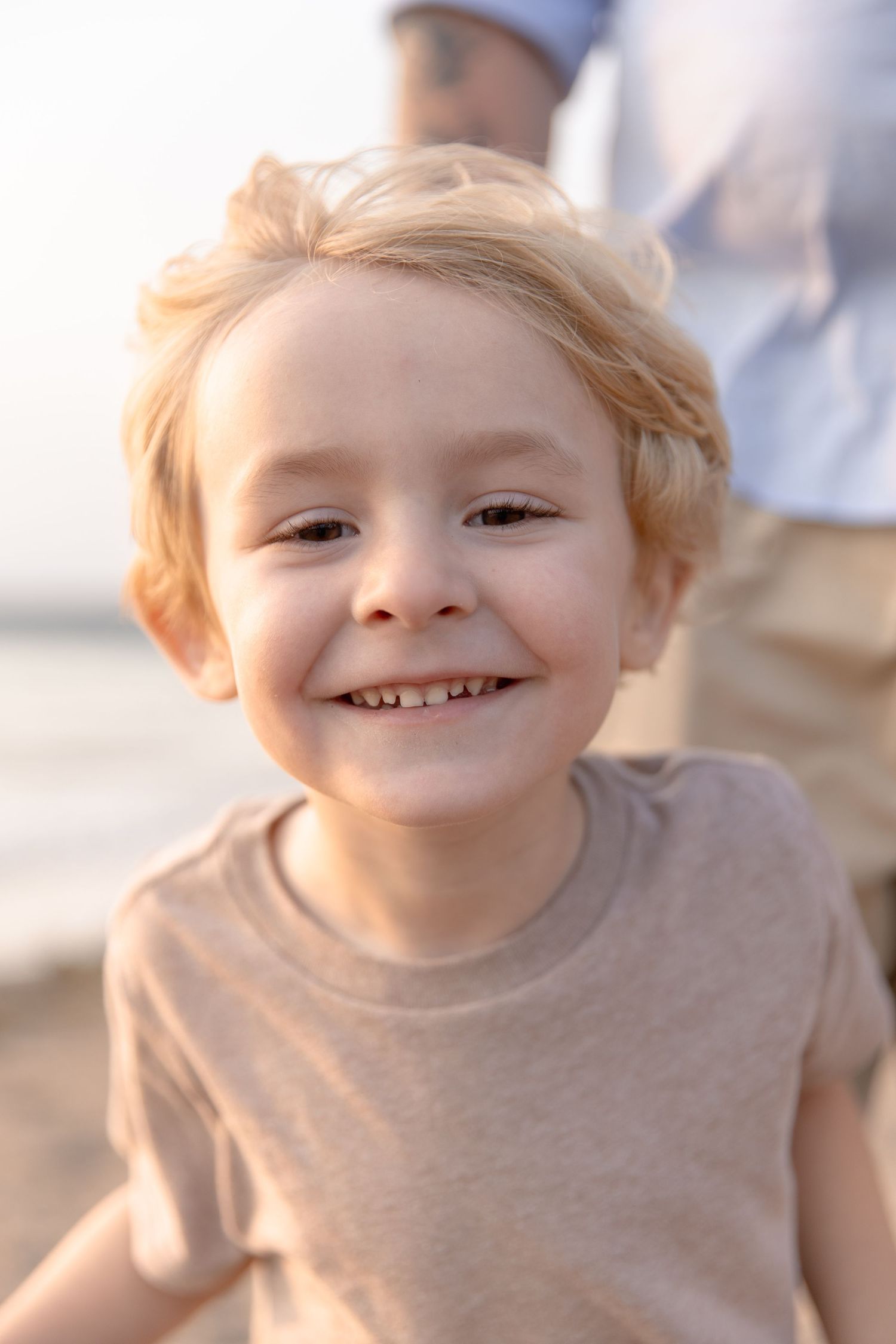 A child with blonde hair wearing a beige t-shirt smiles joyfully in warm sunlight.