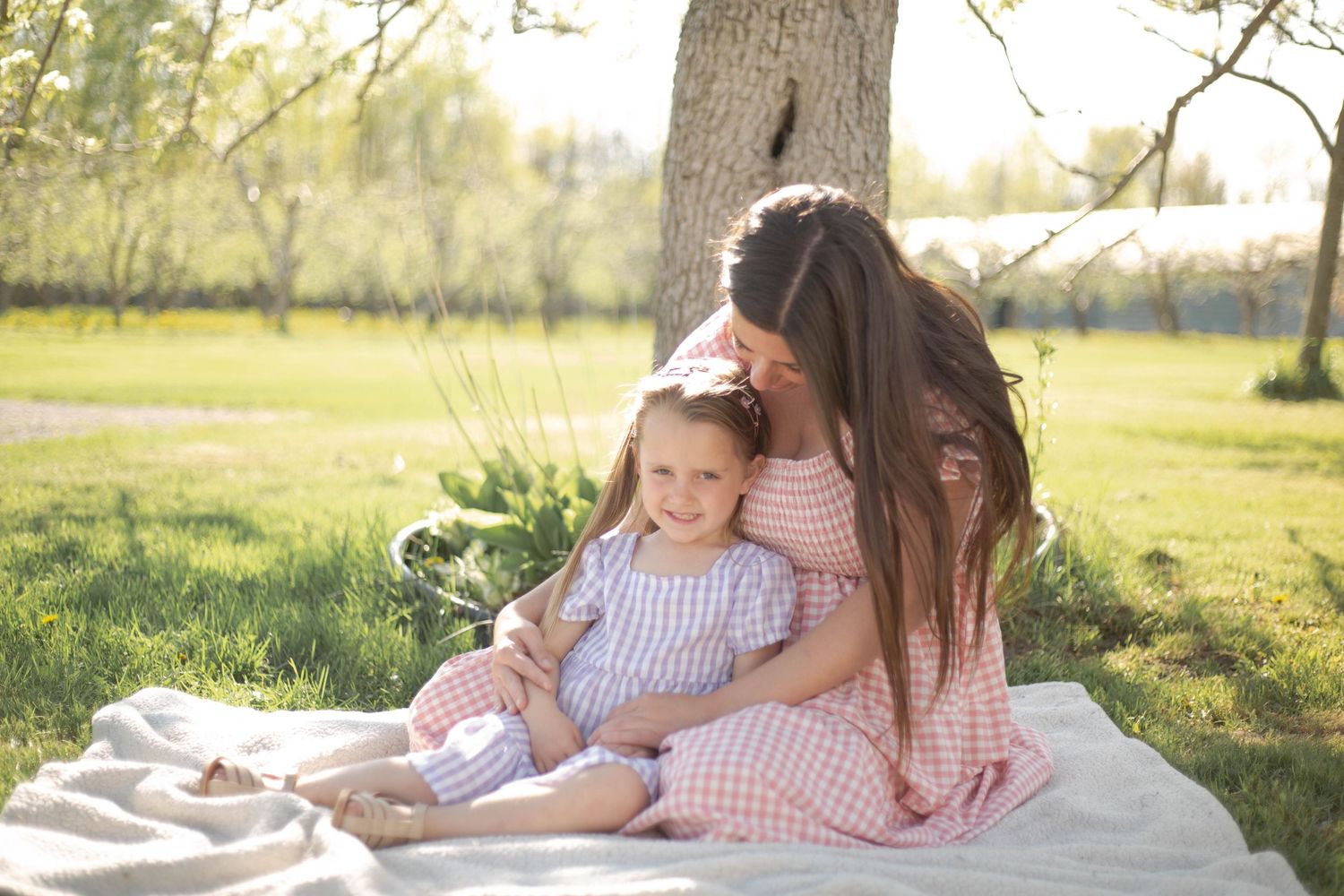 A dreamy outdoor family photography session under a tree during golden hour in a grassy field.