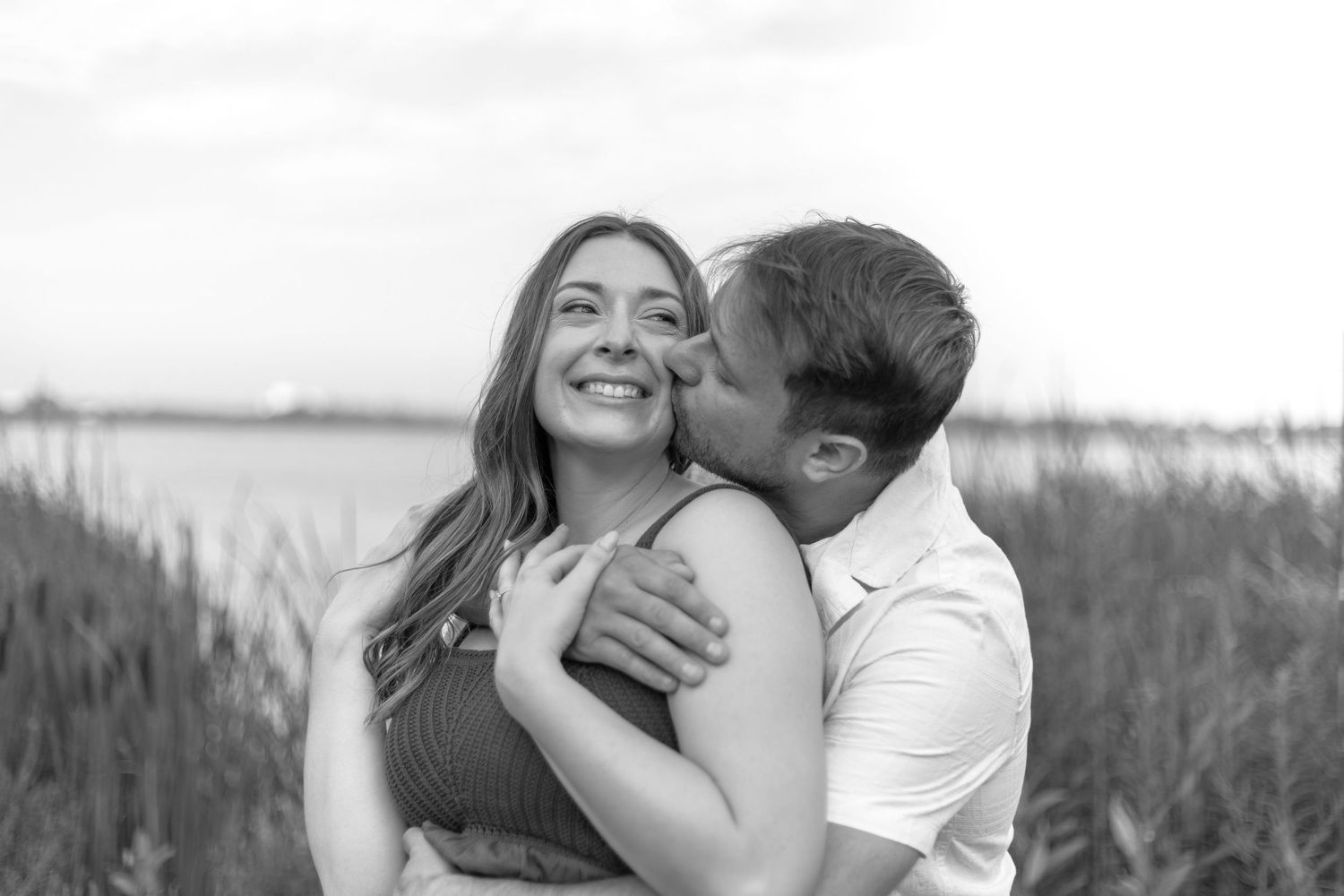 Romantic couple embraces and kisses in a field of tall grass during sunset.