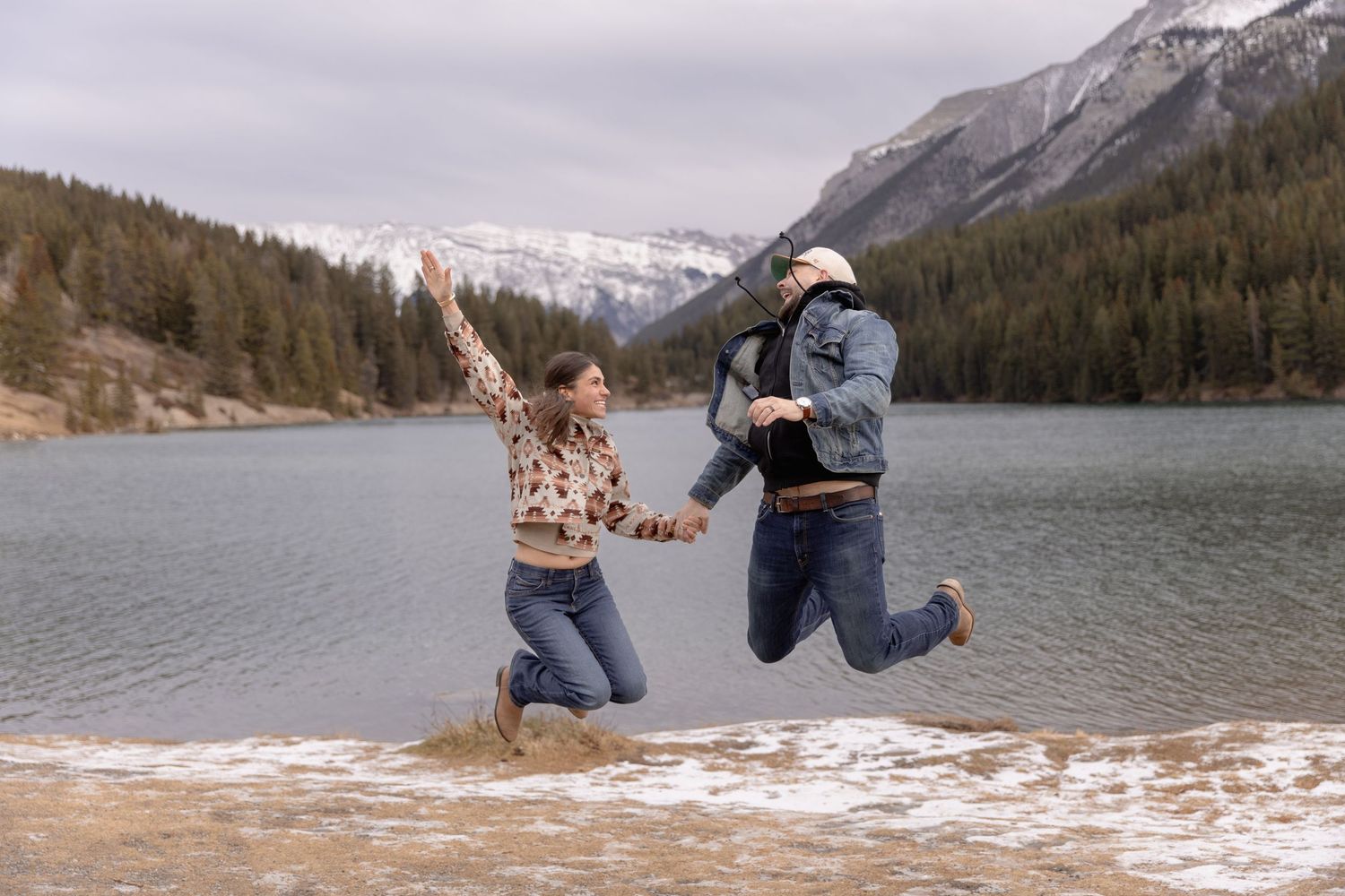 A couple embraces while taking photos against a scenic mountain lake backdrop in the wilderness.