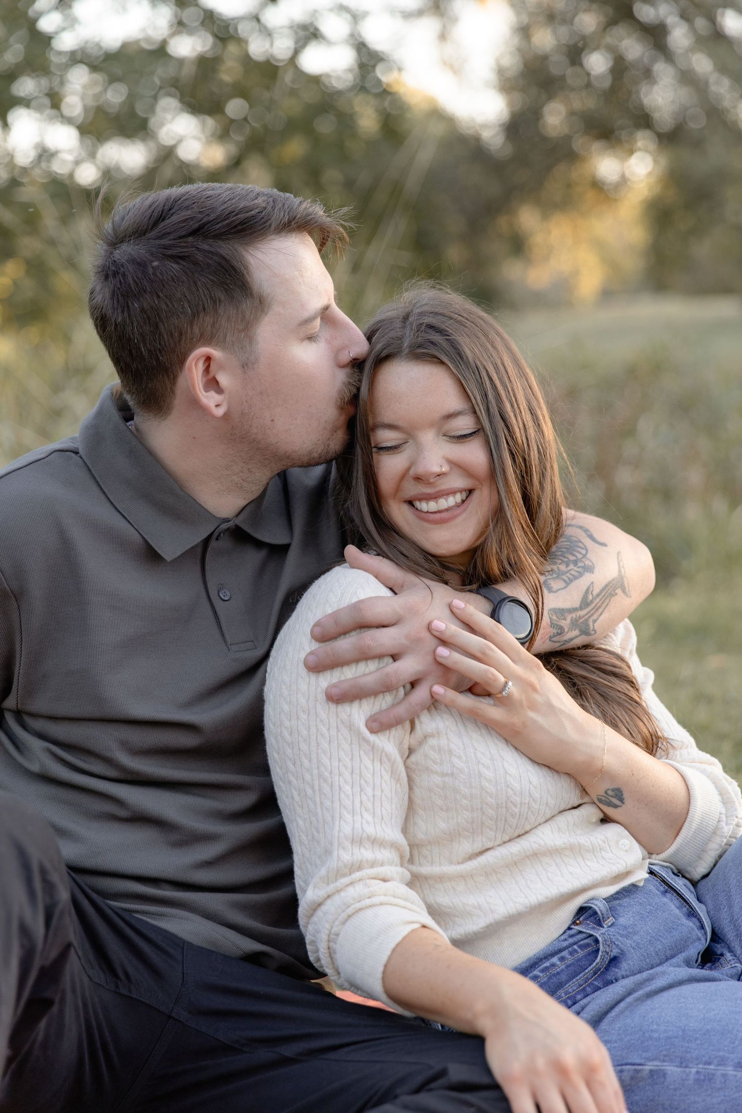 A couple in casual attire shares intimate moments while relaxing outdoors during a photo session at sunset.