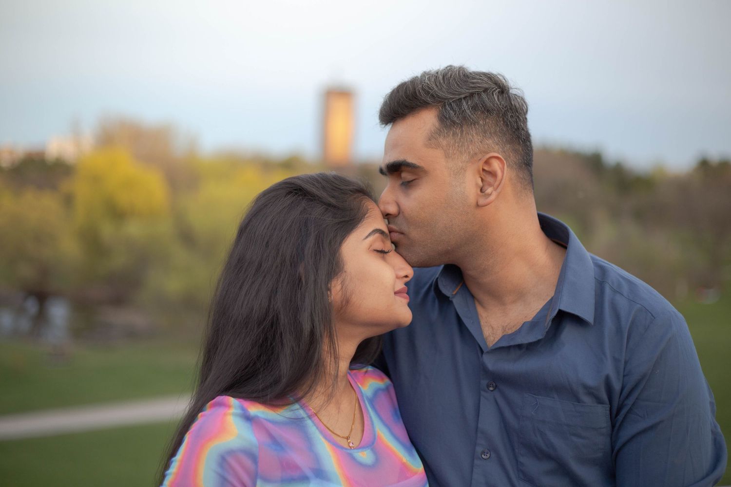 A couple sharing an intimate moment outdoors with blurred autumn foliage in the background.