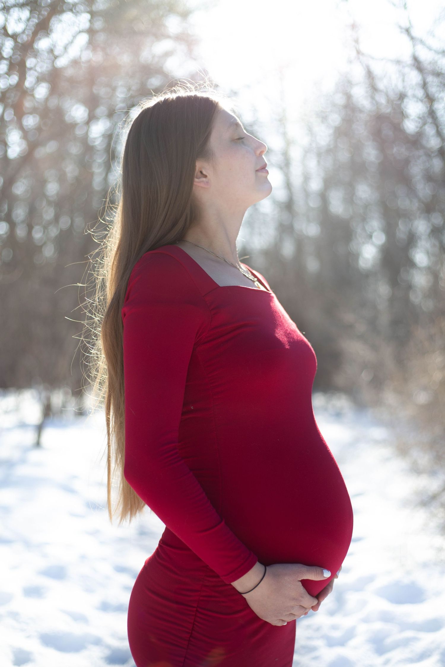 Artistic maternity silhouette against winter sunlight in vibrant red dress.