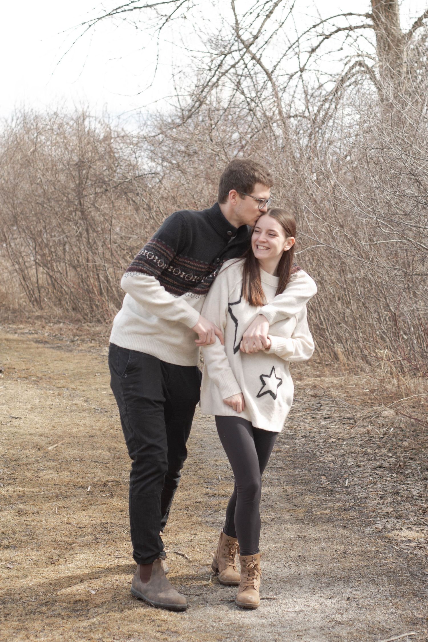 A couple takes a romantic stroll together along a winter trail wearing matching sweaters.