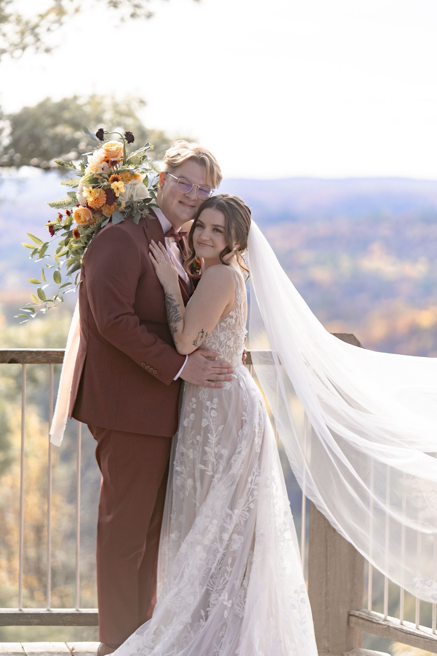 A romantic wedding moment captured on a scenic overlook with fall foliage in the background as a couple shares a kiss.