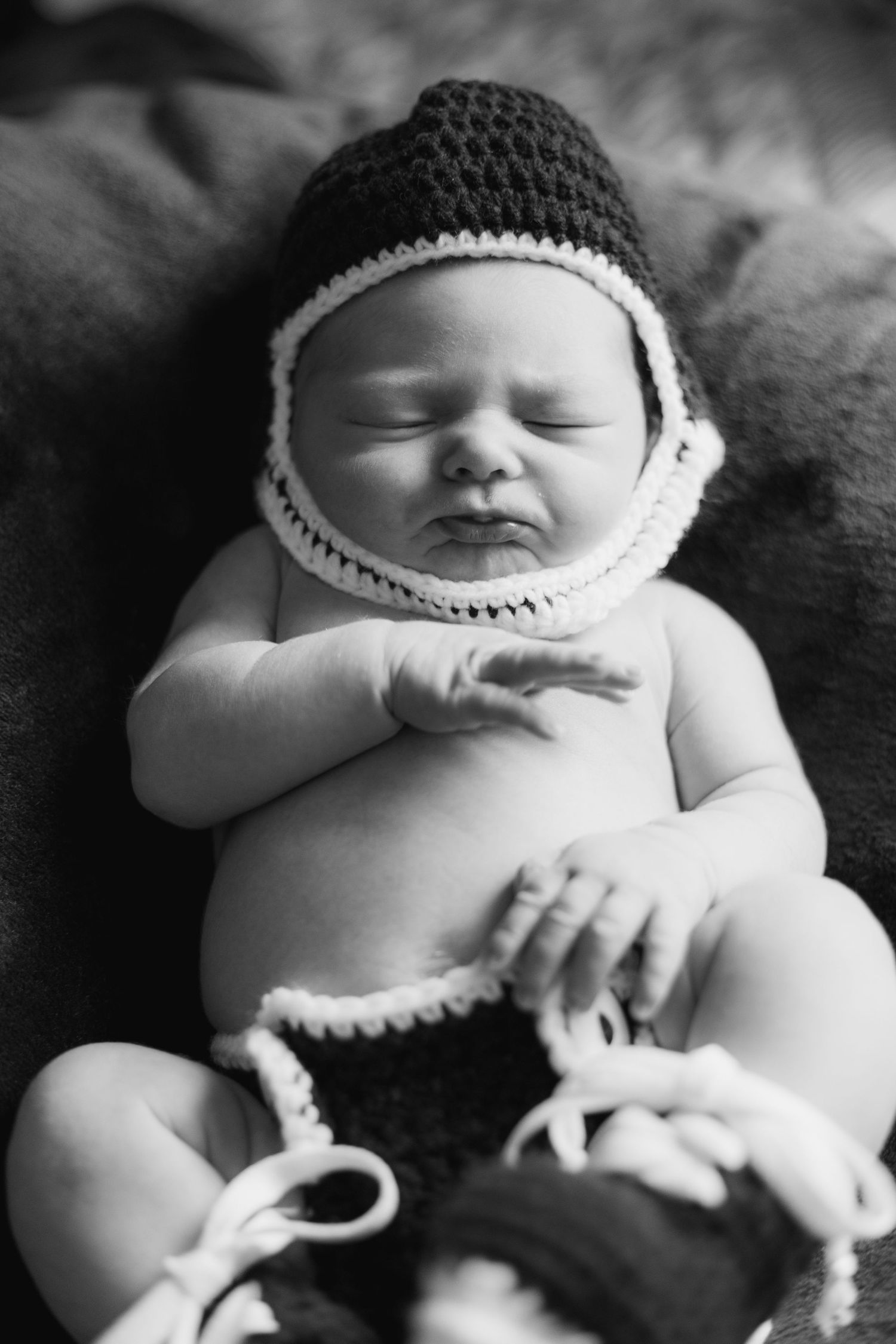 A black and white photo series shows a sleeping newborn baby wearing a small knitted hat against a dark background.