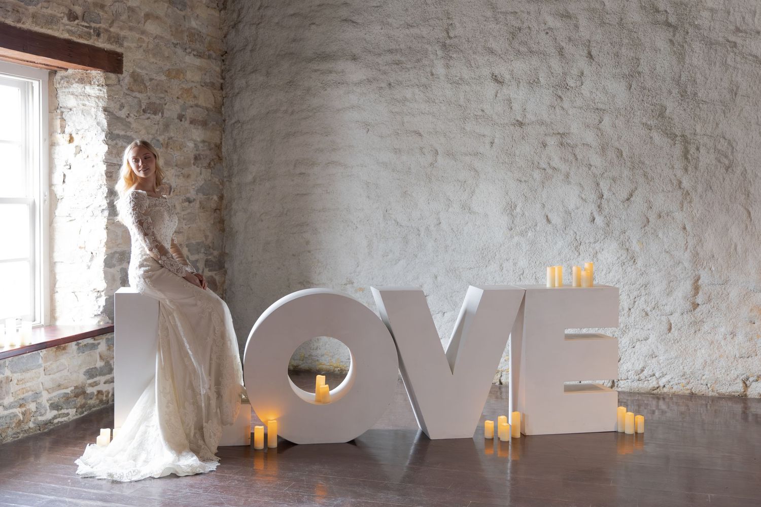 A white love sign decoration sits against a rustic brick wall with glowing candles creating a romantic ambiance.