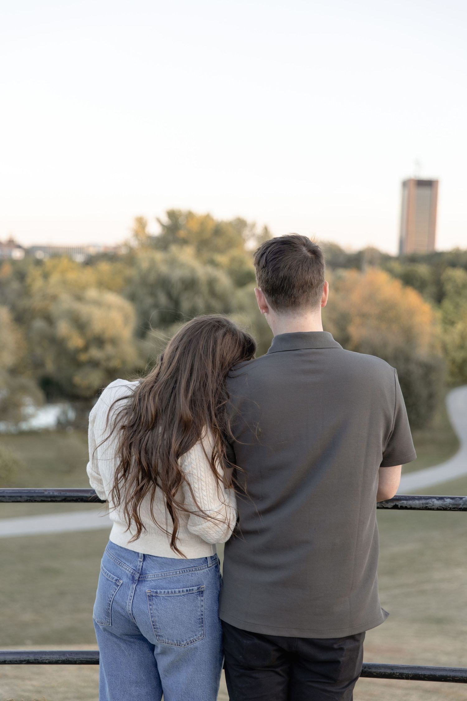 A couple sits together on a railing overlooking a scenic park during golden hour.