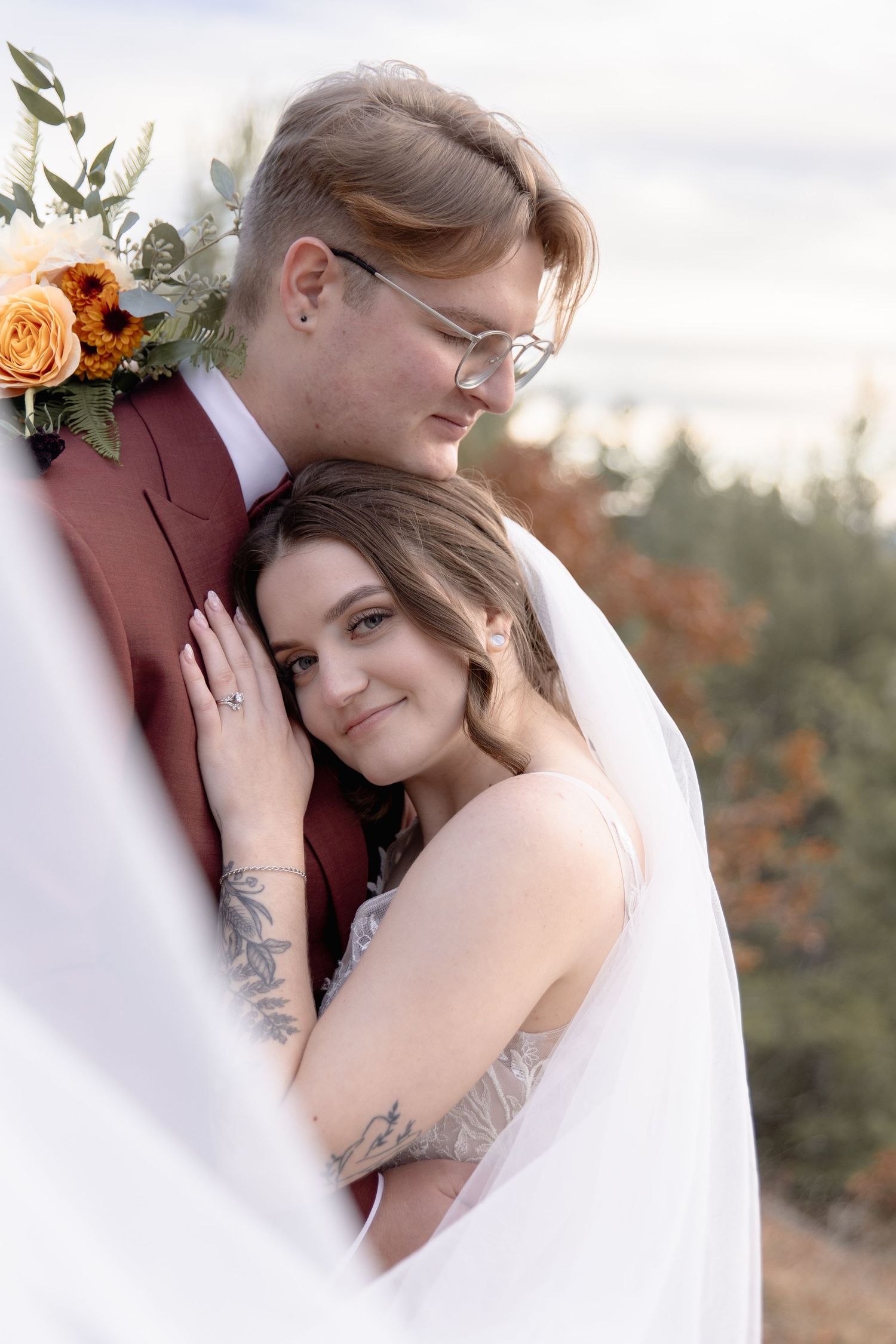 Intimate wedding couple embracing outdoors with autumn foliage in the background.