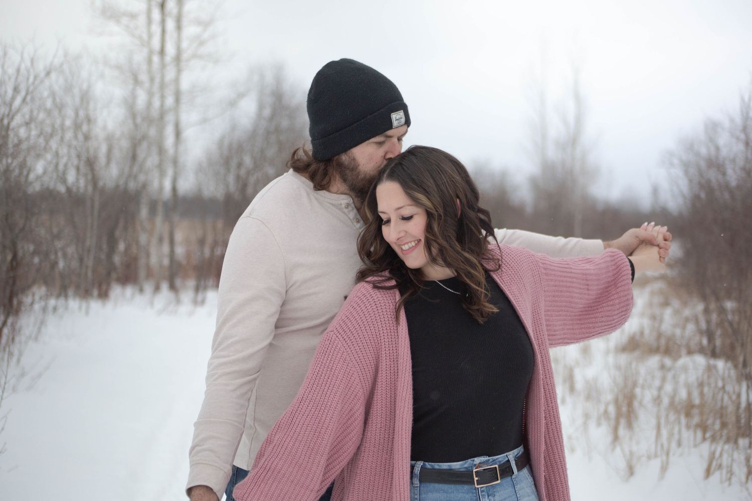 A romantic winter photoshoot featuring a couple embracing in the snow wearing casual winter attire.
