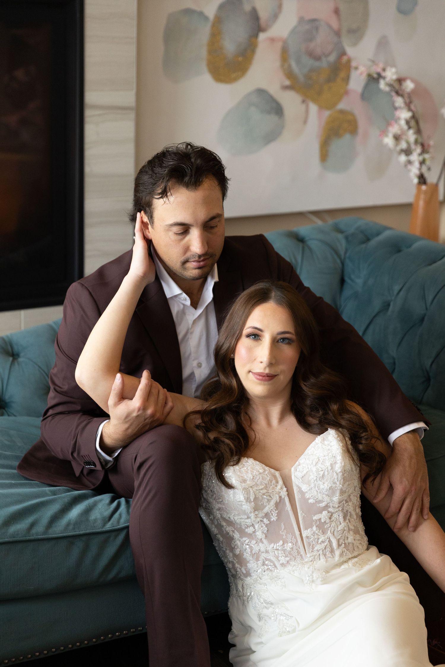 Intimate portrait series of couple in wedding attire posing playfully on teal velvet couch with wall art backdrop.