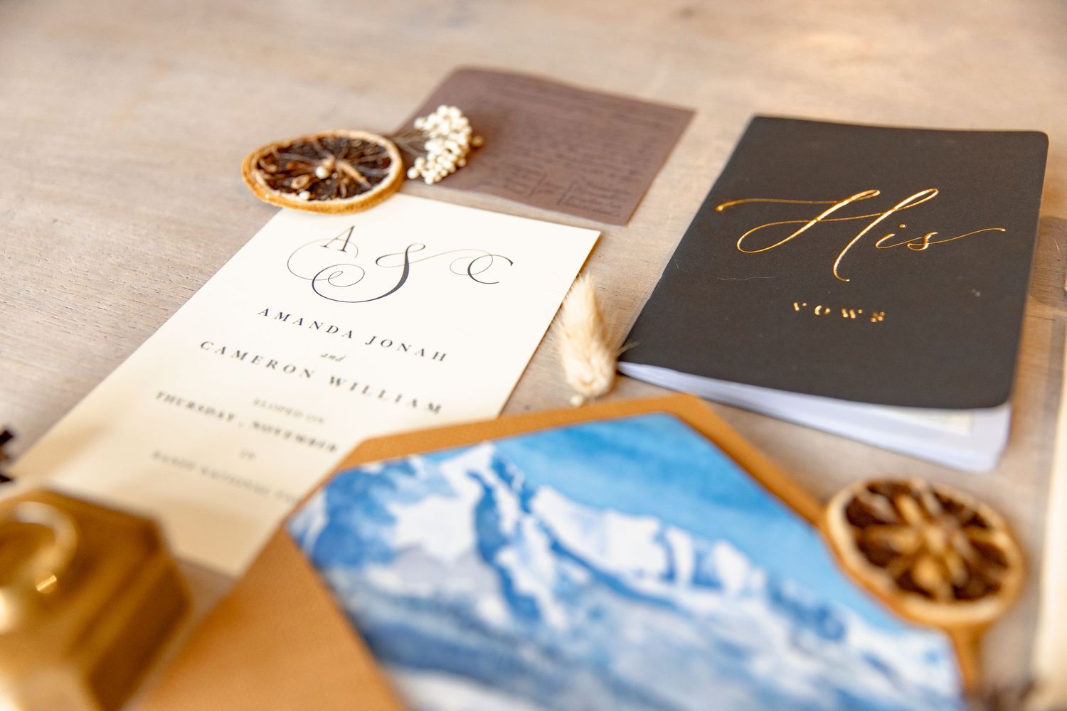 Elegant wedding stationery and invitations with gold calligraphy displayed on a rustic wooden surface.