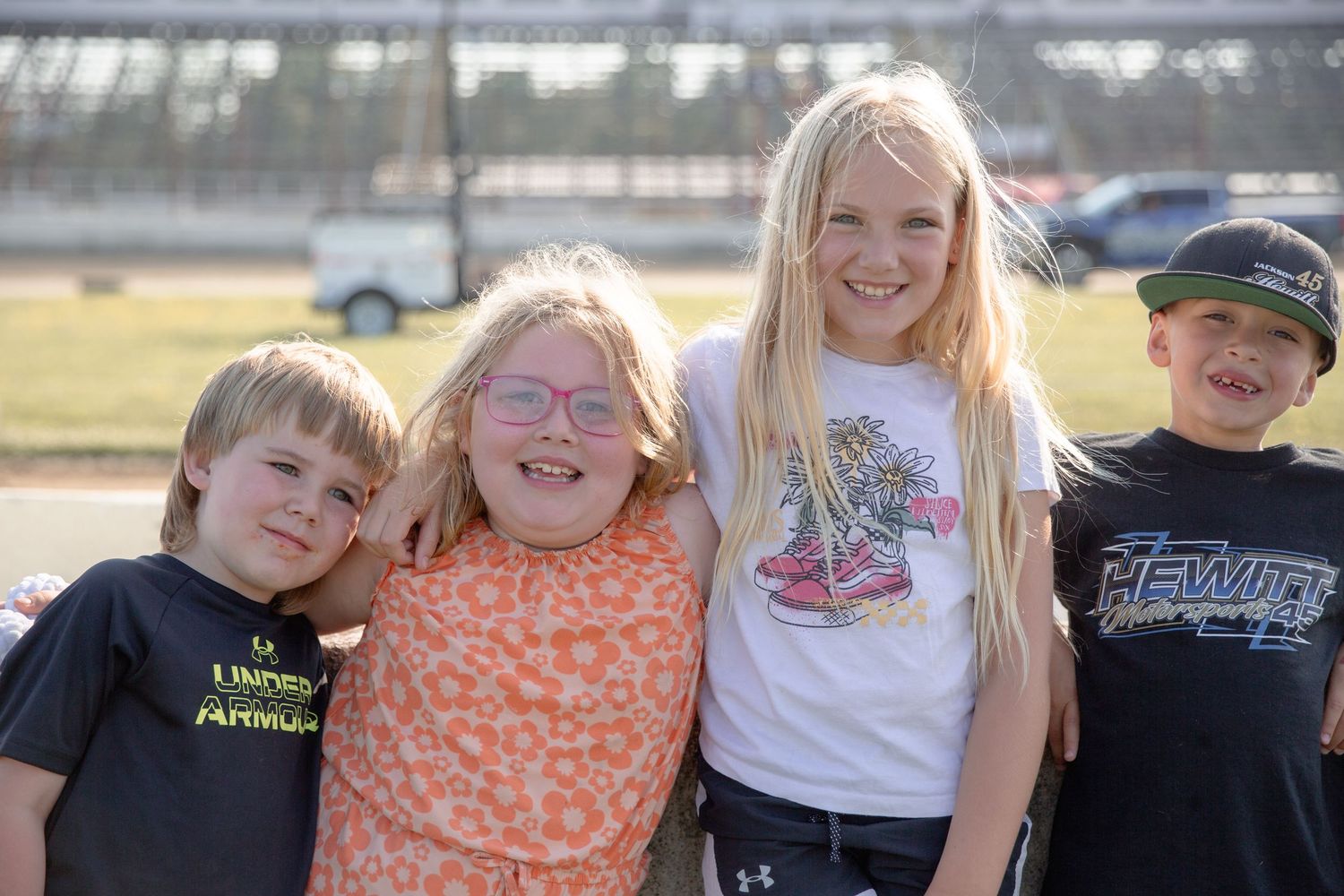 A group of four kids smile together outdoors on a sunny day, showing their joy and friendship.