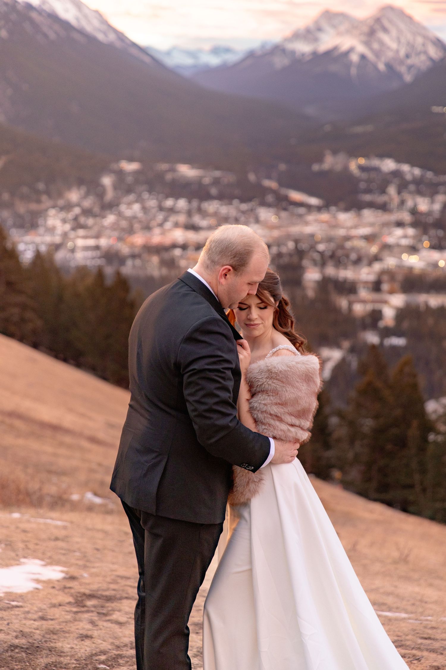 A romantic winter wedding photoshoot in the mountains with snow-capped peaks and a sunset glow in the background.