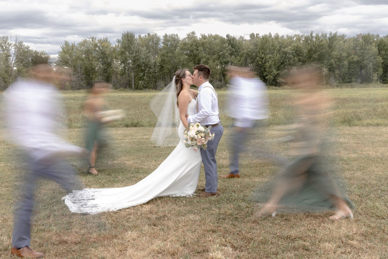 Motion blur captures a couple in a flowing white dress and suit dancing across a rustic outdoor field.