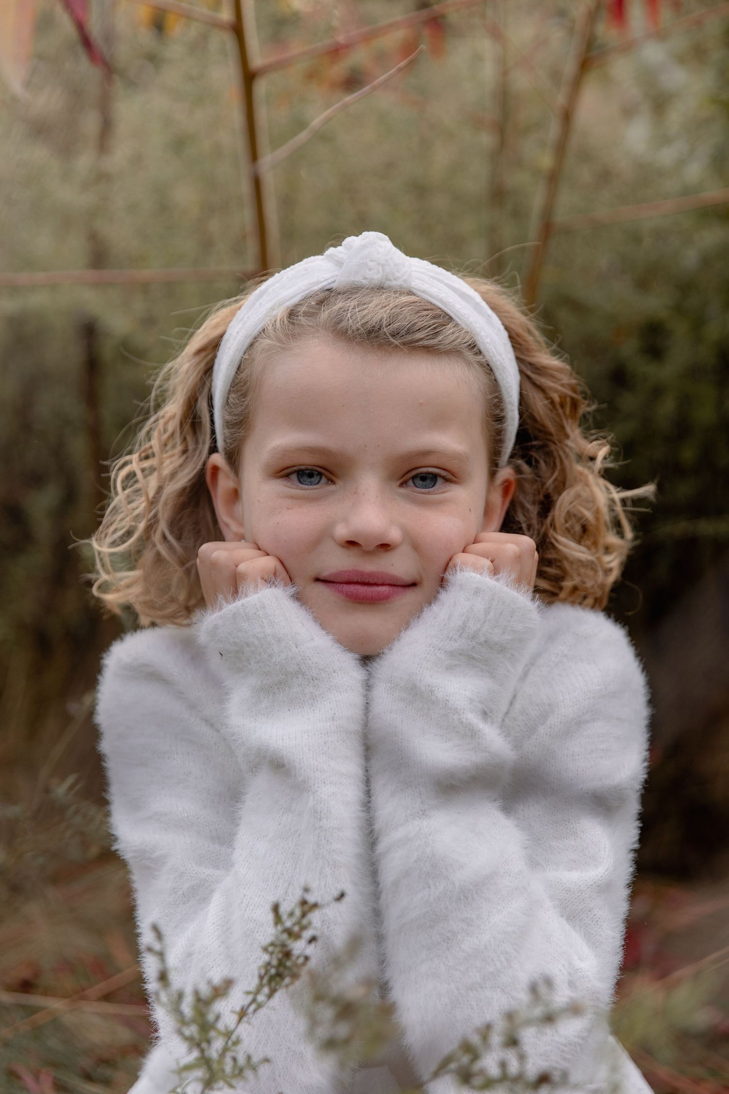 Child wearing white fluffy mittens plays peek-a-boo outdoors in a playful winter portrait series.