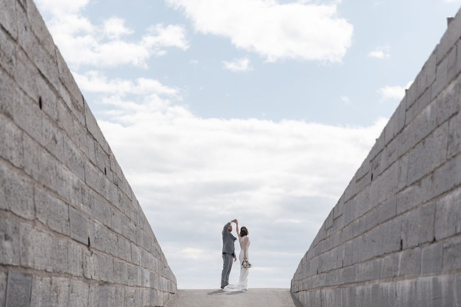 Couple embracing between two large stone walls under a cloudy sky, perfect for a wedding or engagement photo.