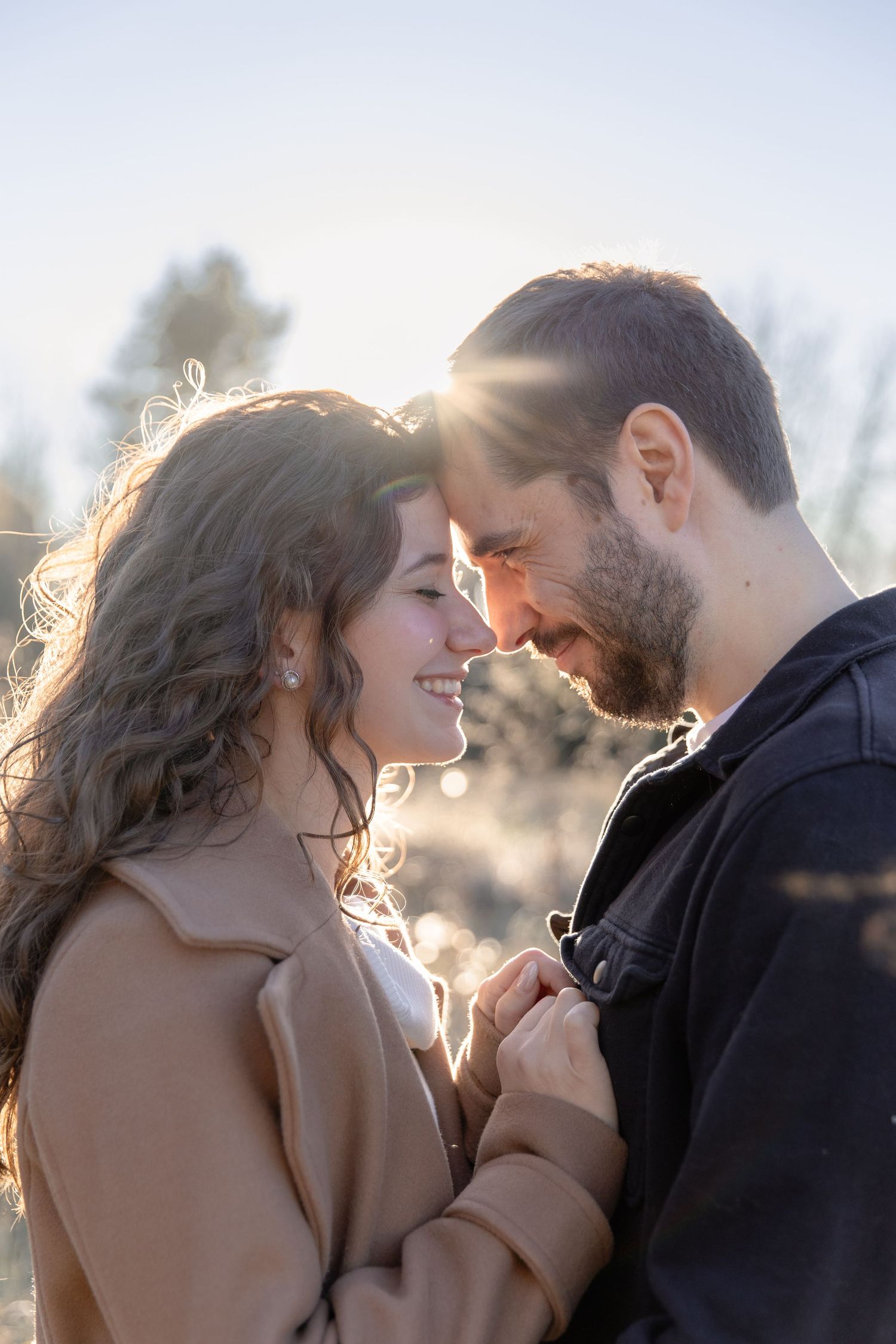 Romantic couple sharing intimate moment at sunset with sunlight creating backlit glow through their hair.