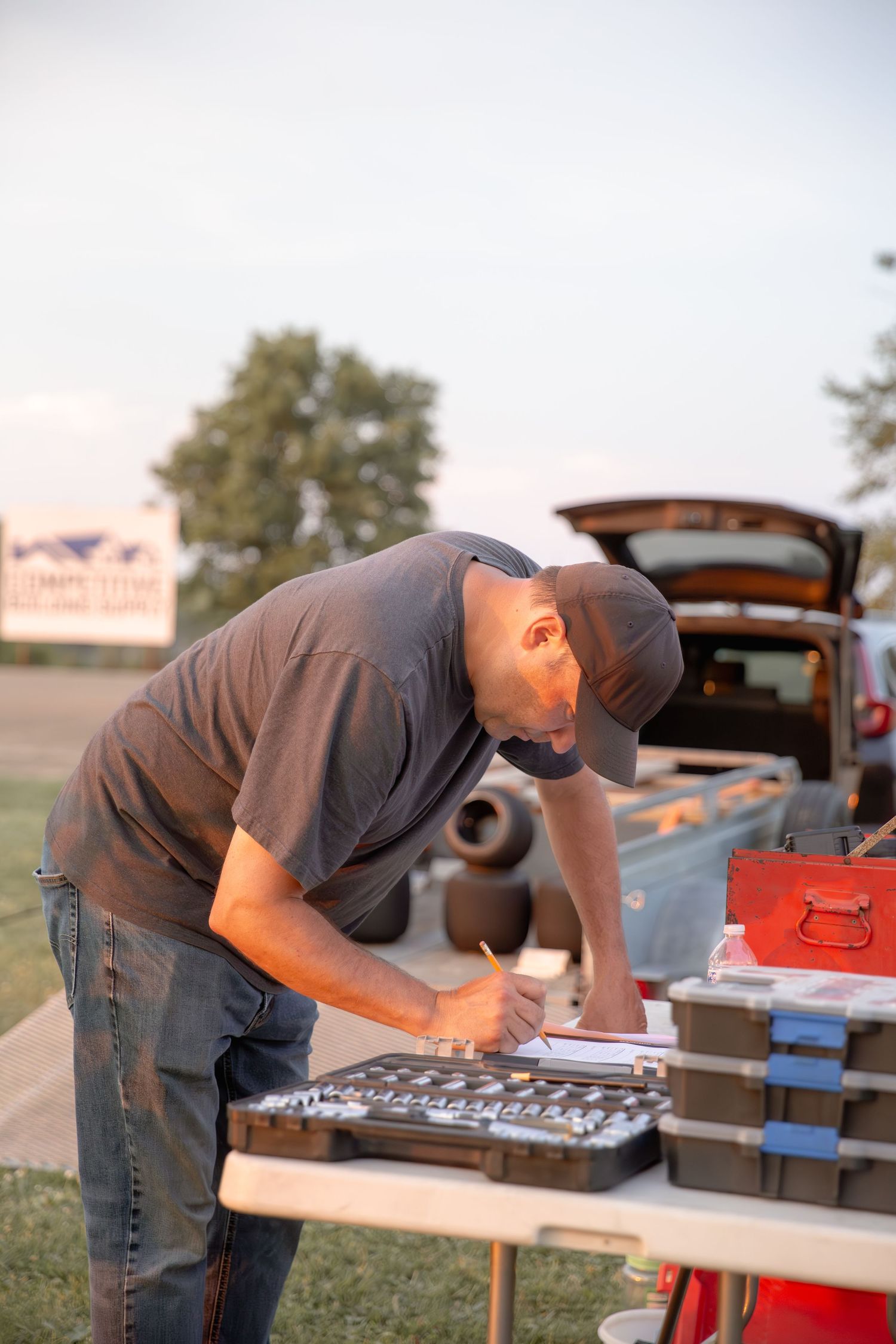 A person in a gray shirt examines and works on items laid out across a folding table outdoors.
