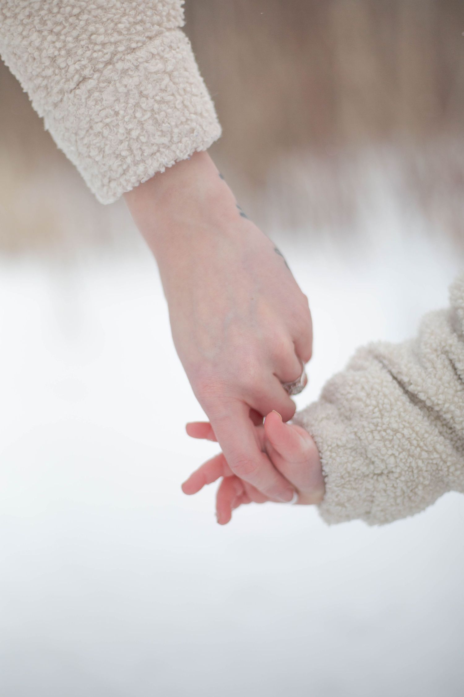 Baby holds mom's finger against a snowy winter backdrop.