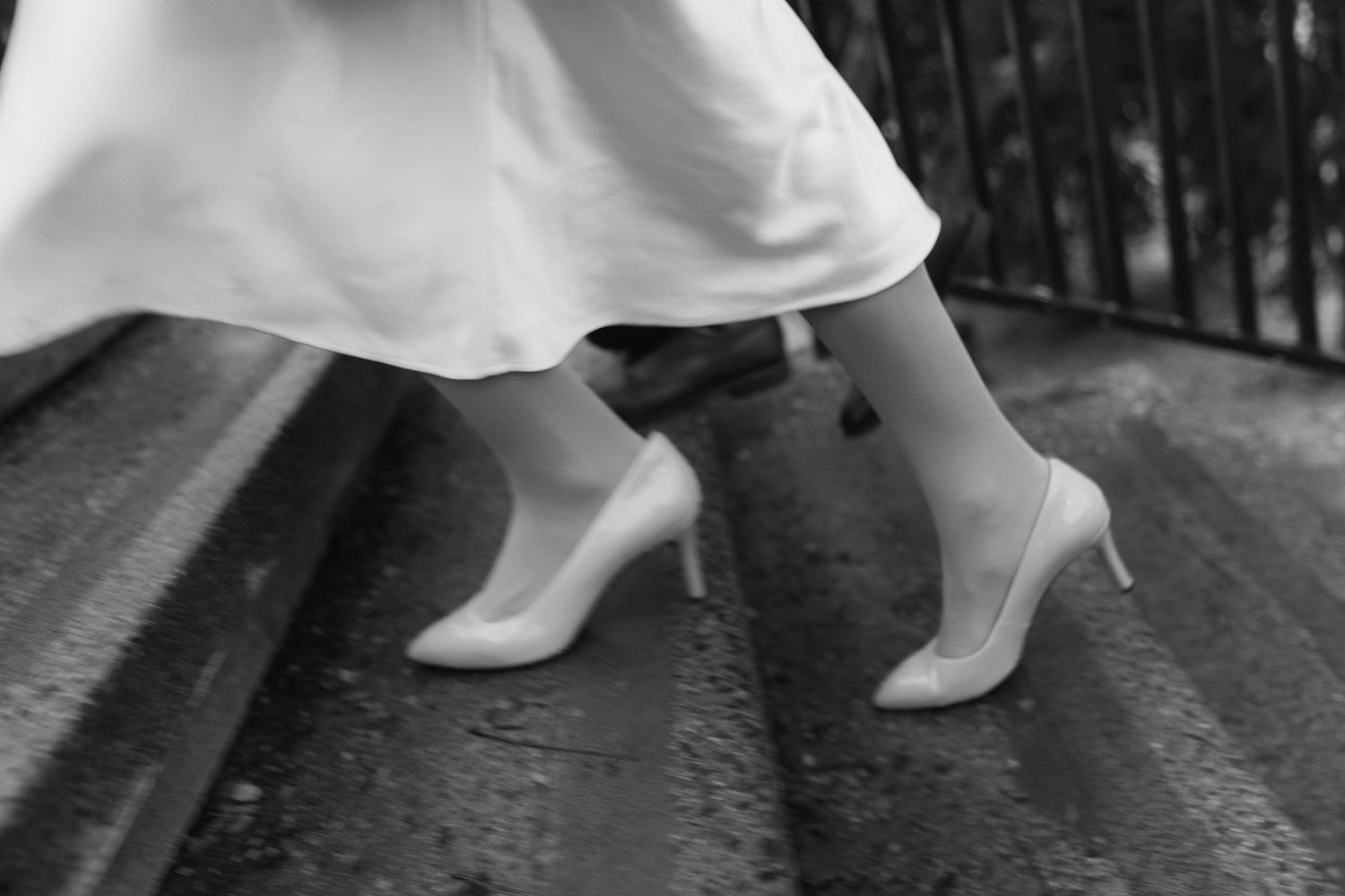 Close-up of feet climbing stairs with white dress and formal shoes on stone ground.