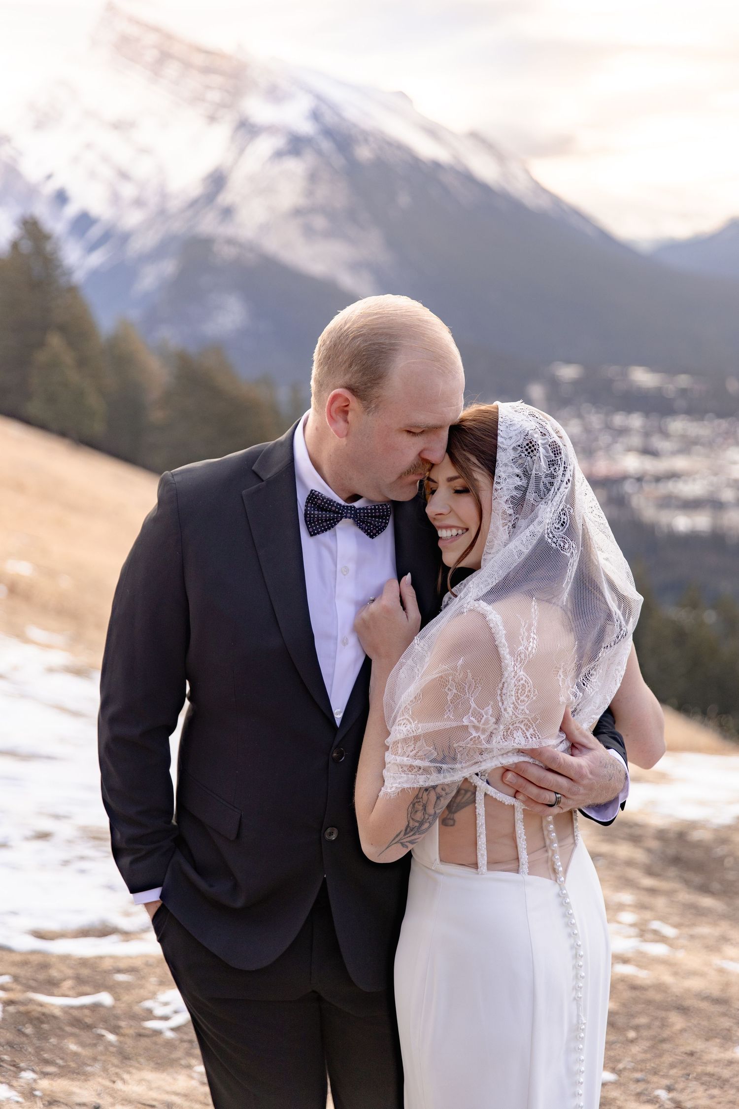 A couple shares an intimate moment during their winter mountain wedding in Colorado with snowy peaks in the background.
