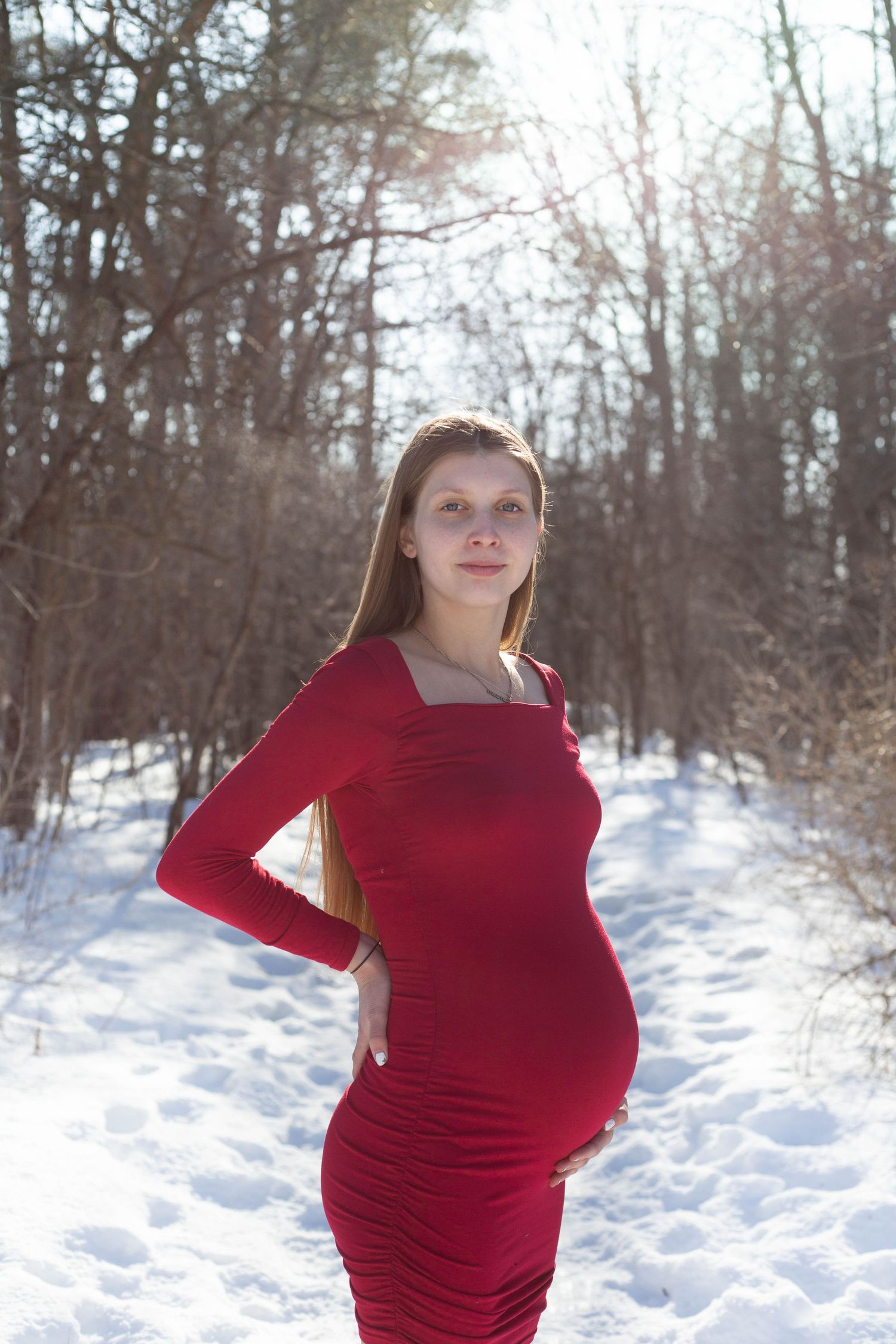 Radiant winter maternity portrait with red fitted dress in snow-covered setting.