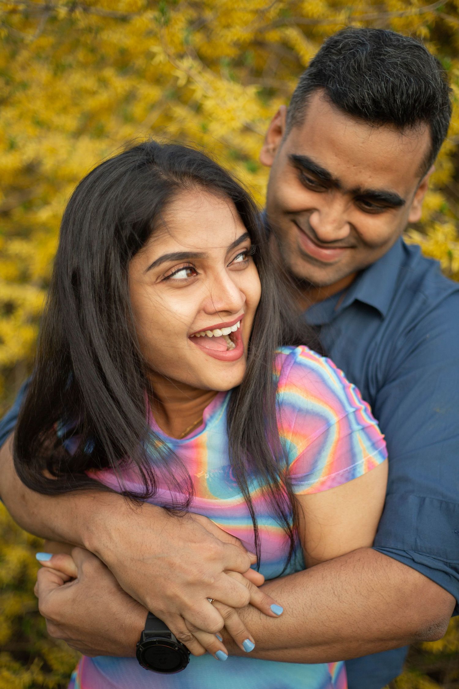 A happy couple embraces outdoors against a backdrop of golden autumn foliage, with one wearing a colorful striped shirt.