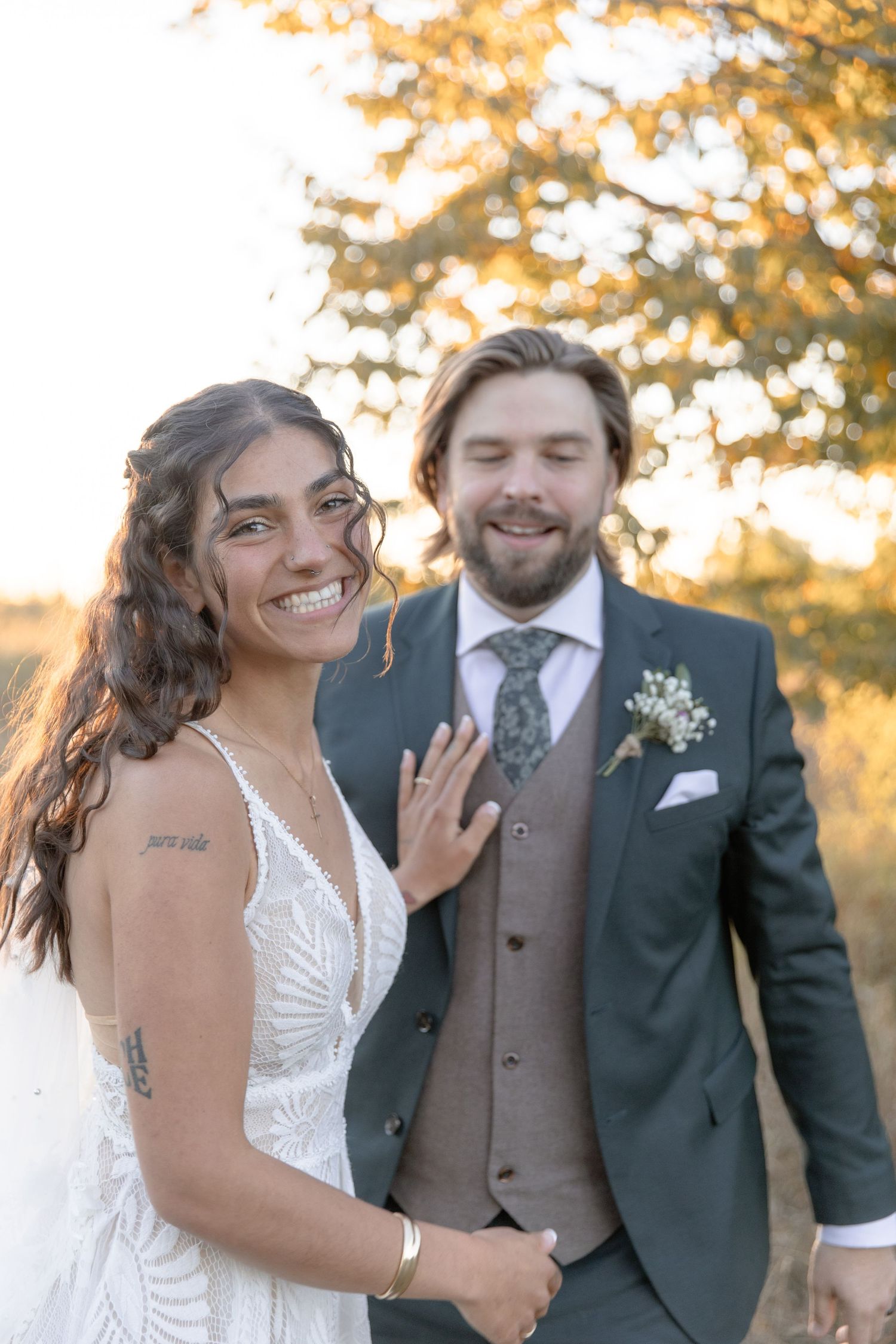 A happy couple shares joyful candid moments during their autumn wedding photoshoot with golden sunlight in the background.