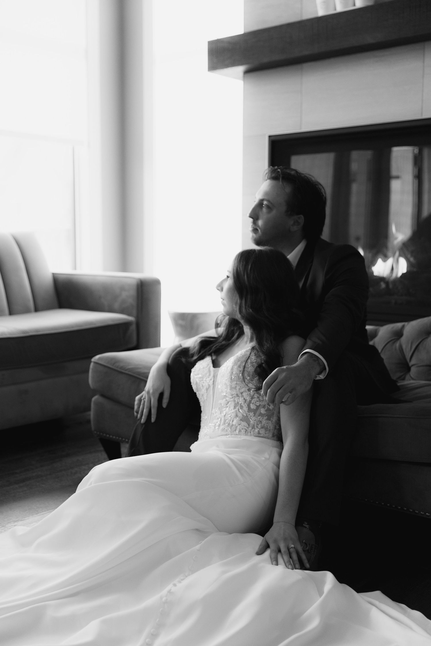 Romantic black and white photo series showing couple lounging together on white couch in elegant wedding attire.