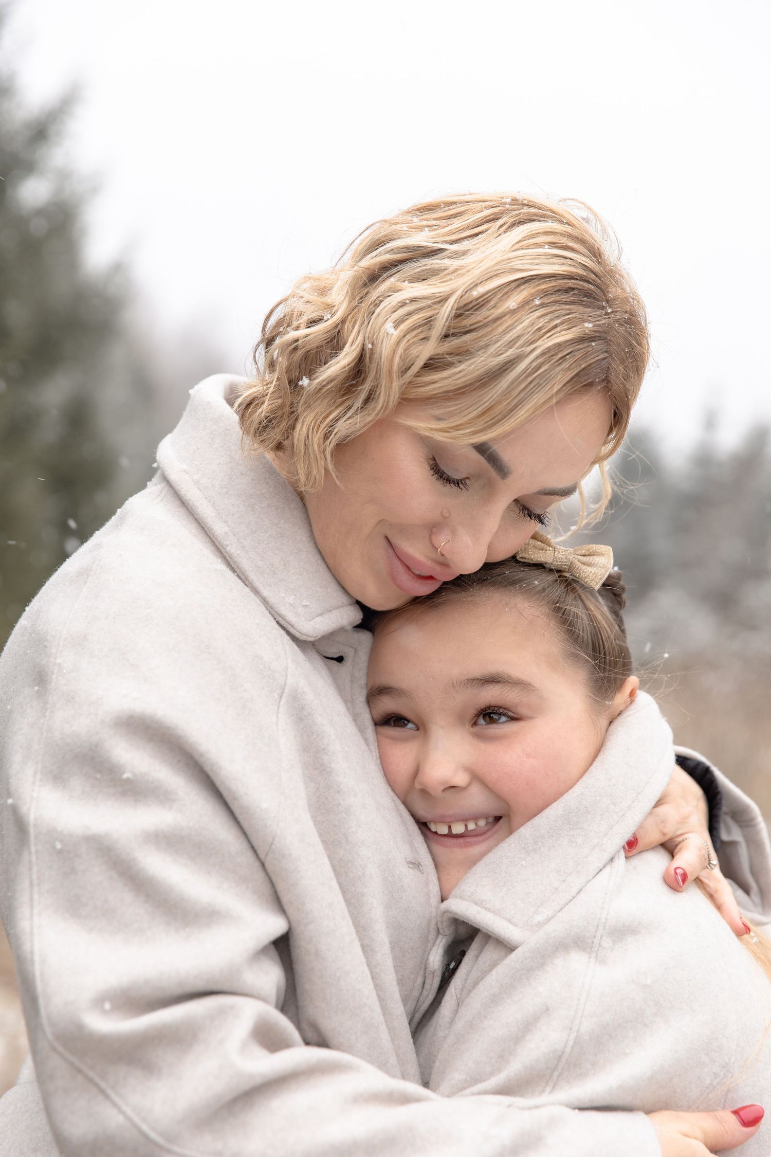 A tender embrace between parent and child wearing white winter clothing in a snowy outdoor setting.