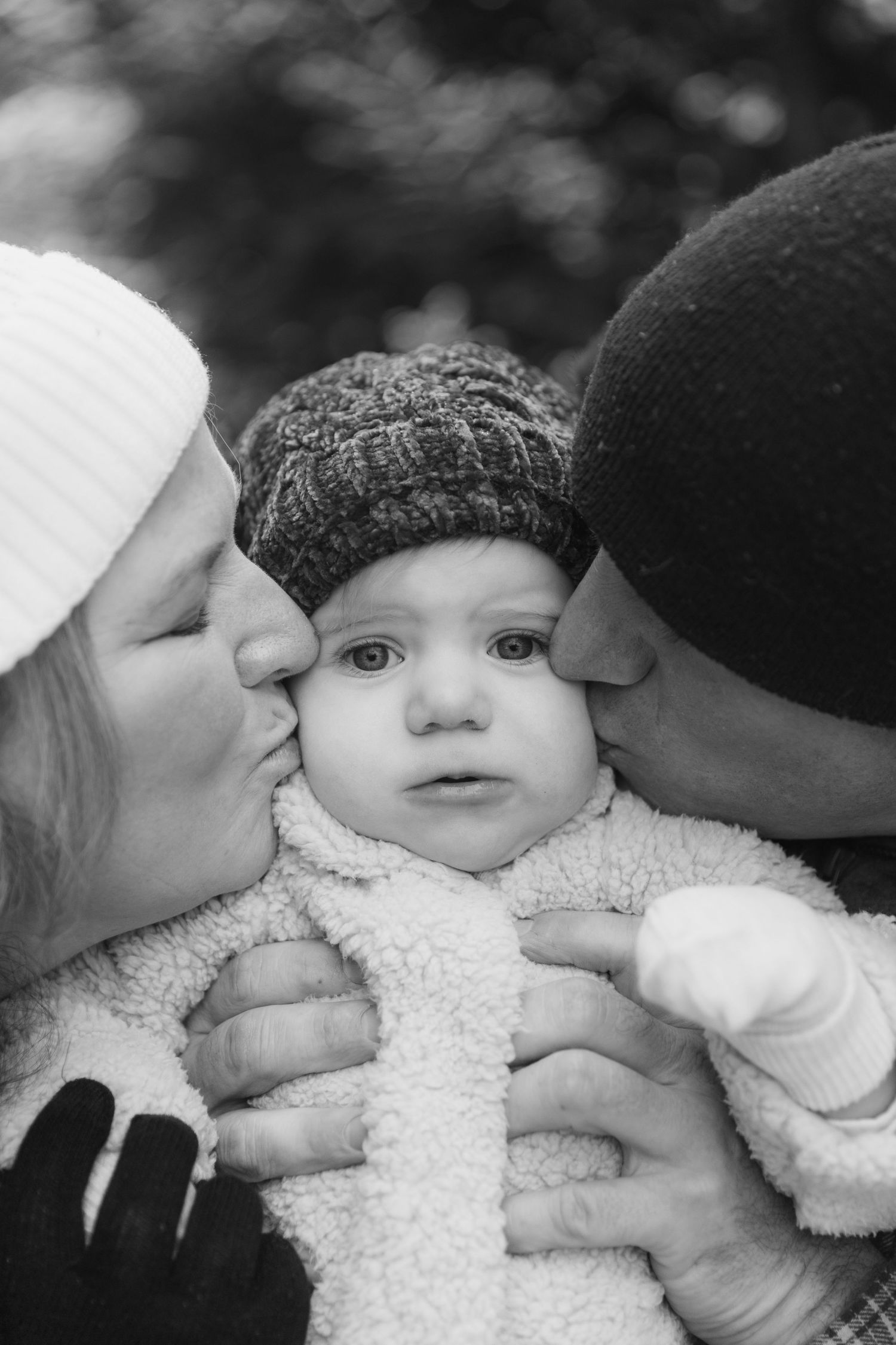 A sweet black and white photo sequence showing parents kissing their baby's cheeks from both sides.
