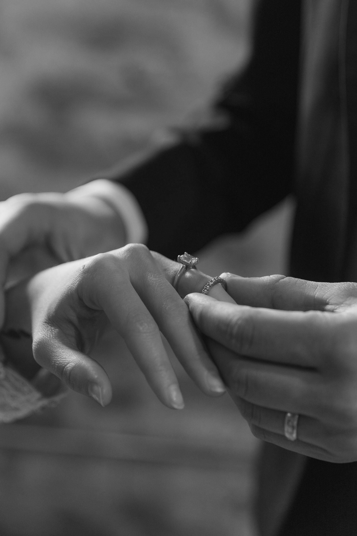 A close-up black and white photograph shows hands exchanging wedding rings during a ceremony.