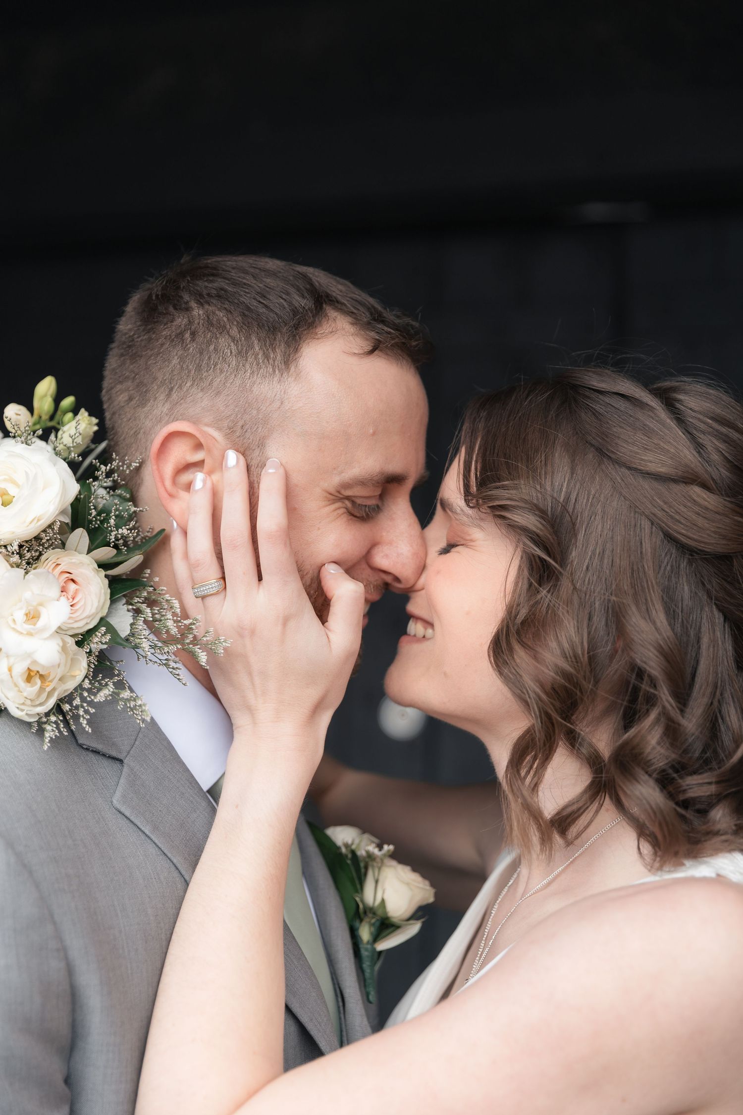 A bride and groom share a romantic almost-kiss moment, with the bride smiling and touching the groom's face on their wedding day.