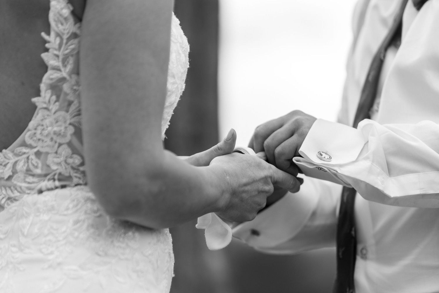 A close-up black and white photo of hands exchanging wedding rings during a marriage ceremony.