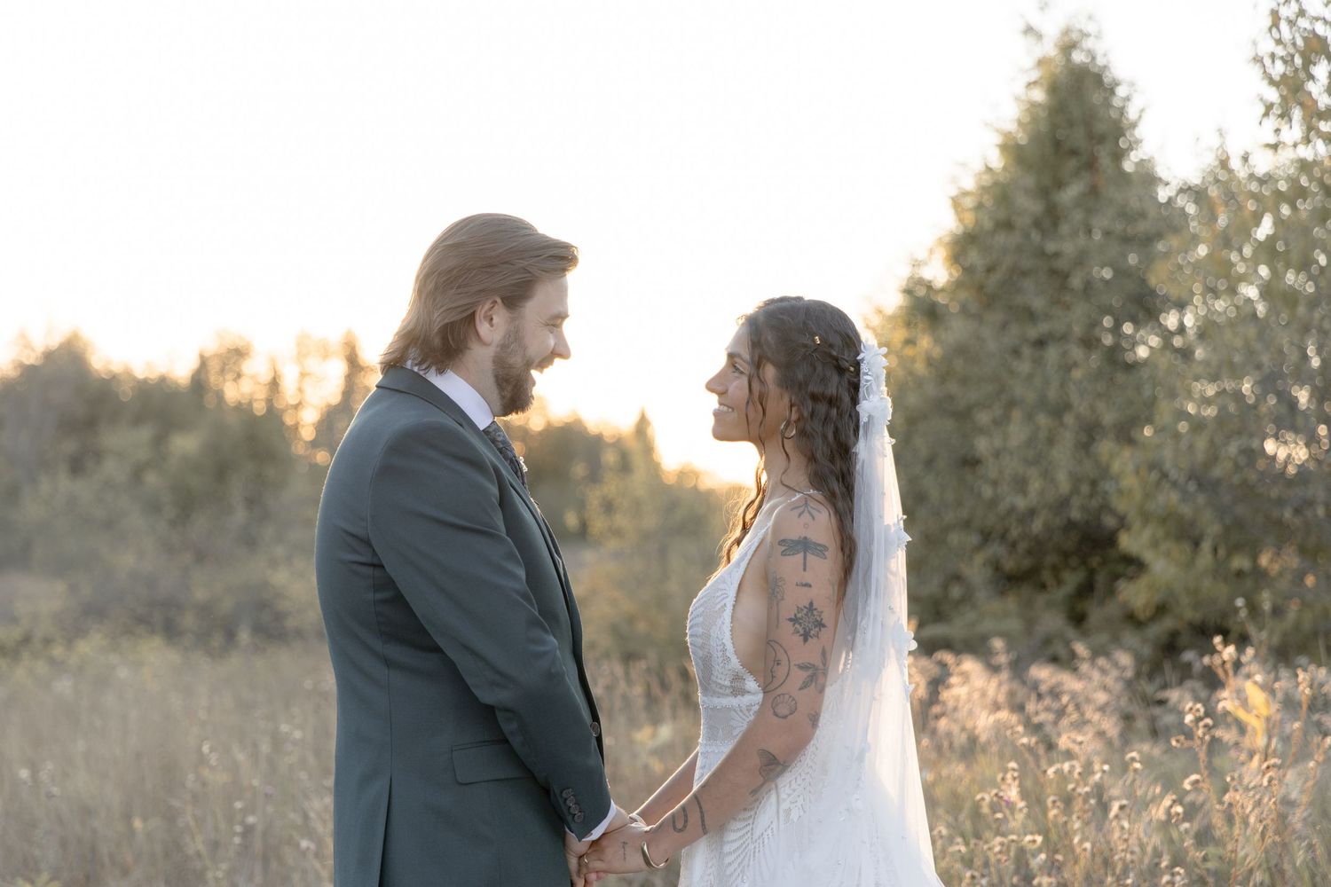 A romantic couple in wedding attire embraces in a golden sunlit field during sunset.