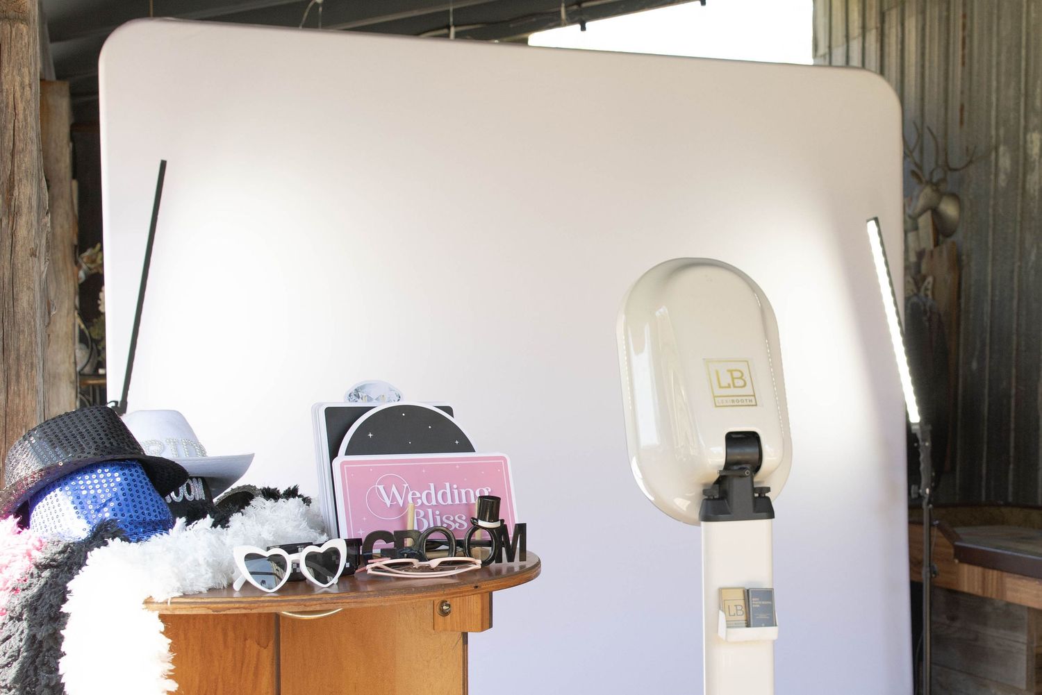 A white photo booth setup with sunglasses and other props displayed on a wooden table in front.